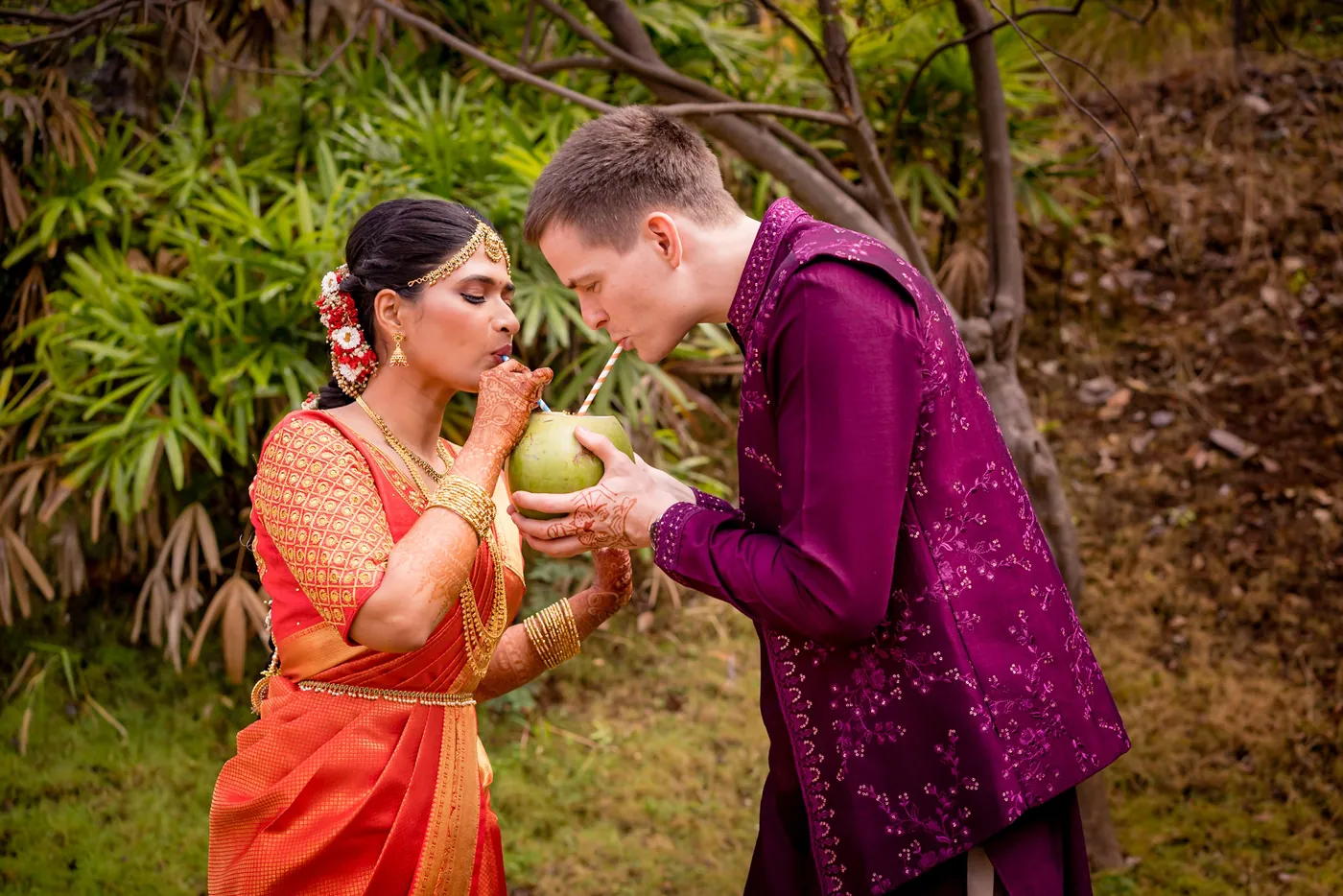 Medha and Stefan share fresh coconut water through straws among green foliage