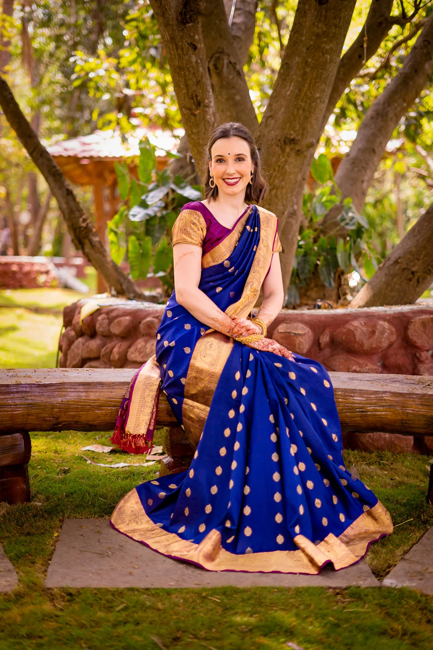 Stefan's sister sits on a carved log bench in a blue sari with her hands in her lap