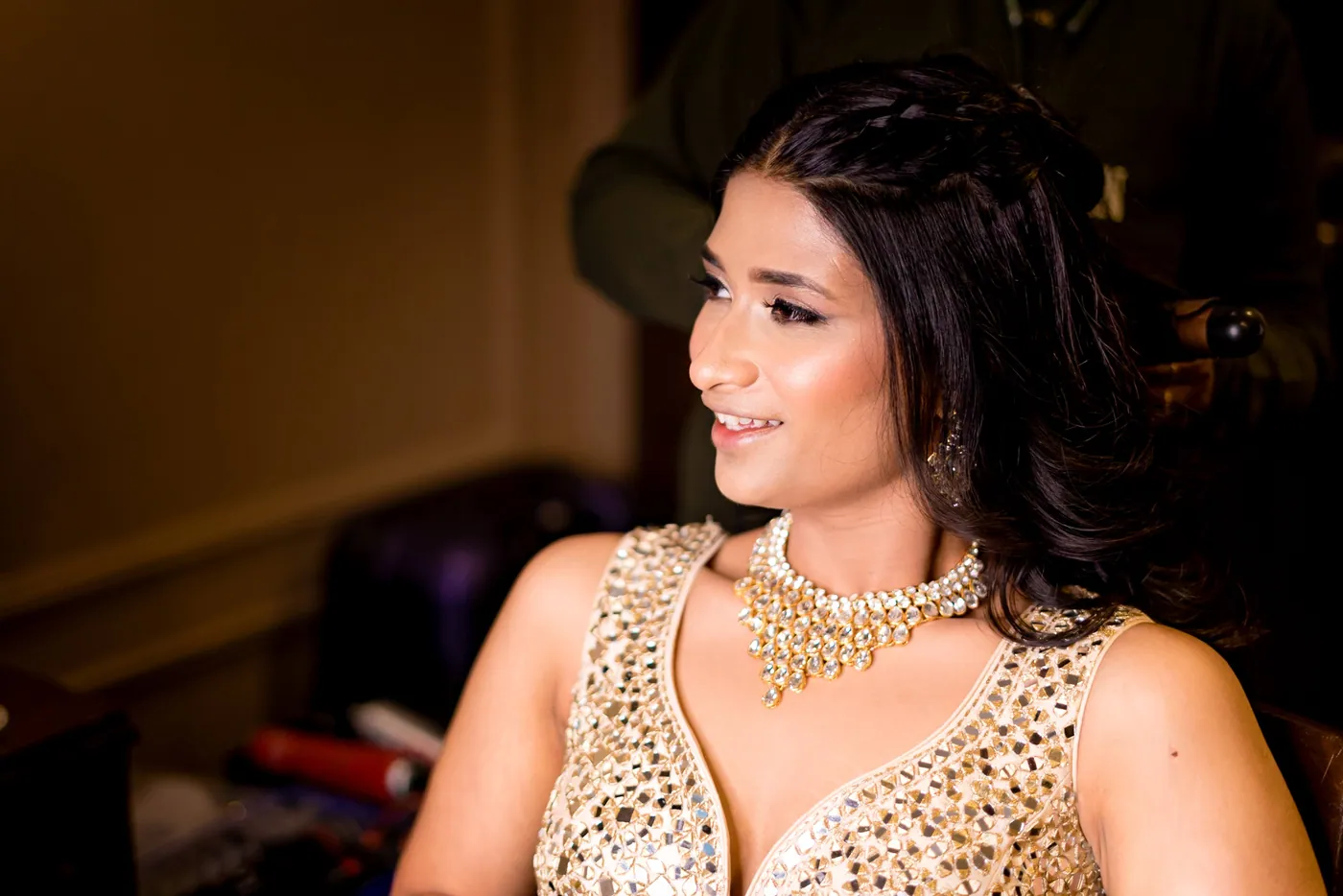 Medha in a gold embellished top looks away from the camera with a layered necklace catching the light