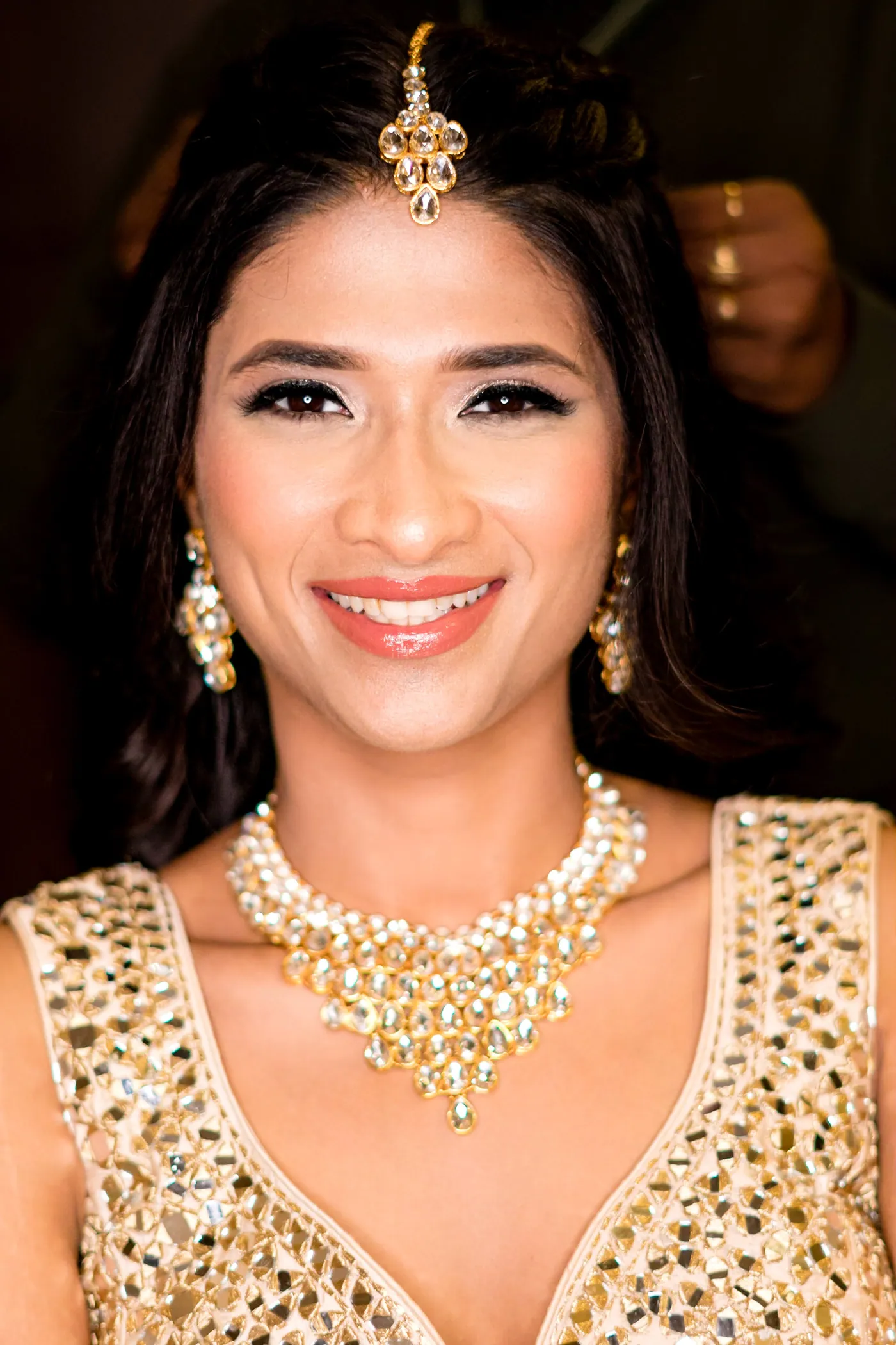 Medha smiles straight at the camera in a tikka, chandelier earrings and a statement necklace
