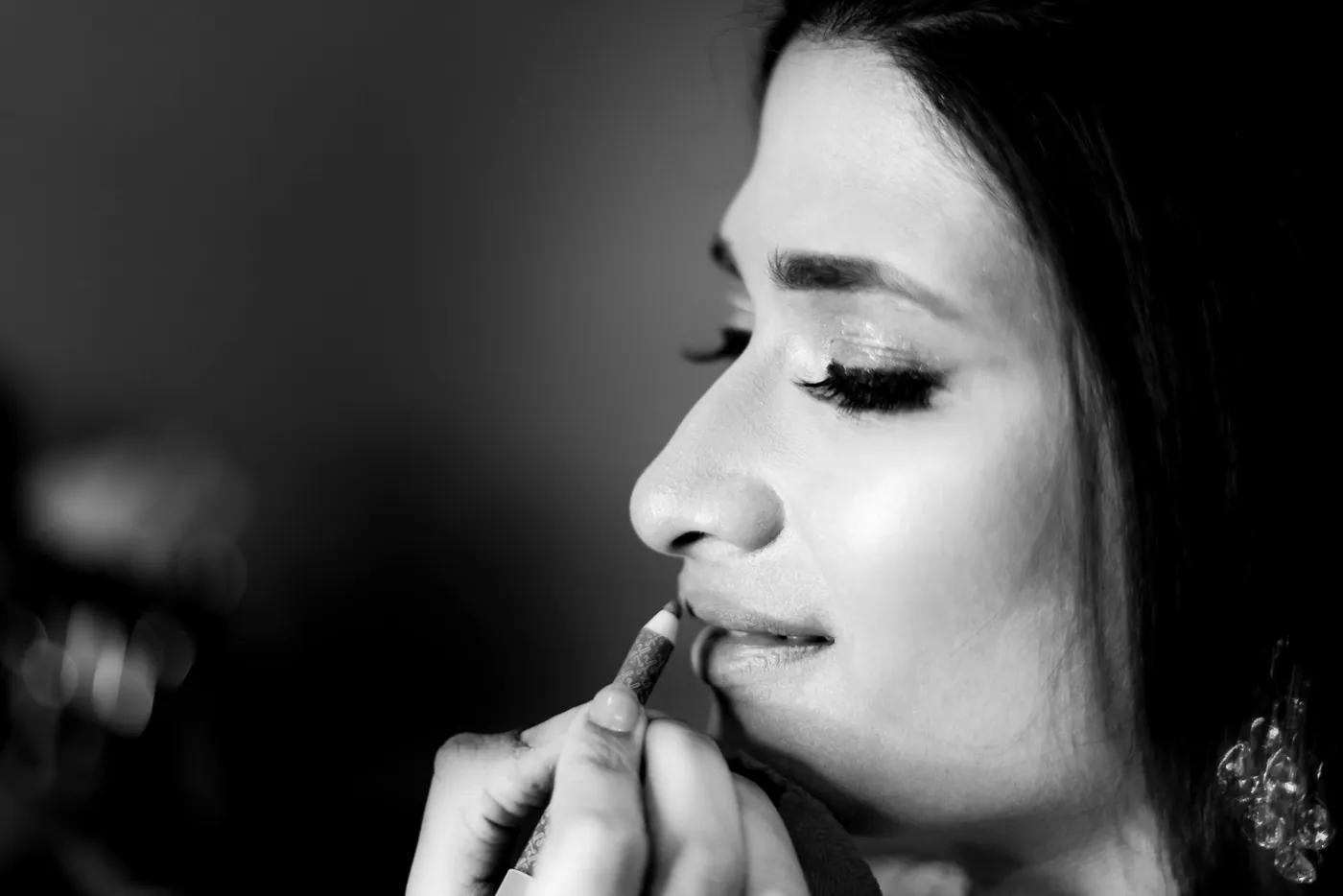 In black and white, Medha in close profile as a hand applies colour to her lips