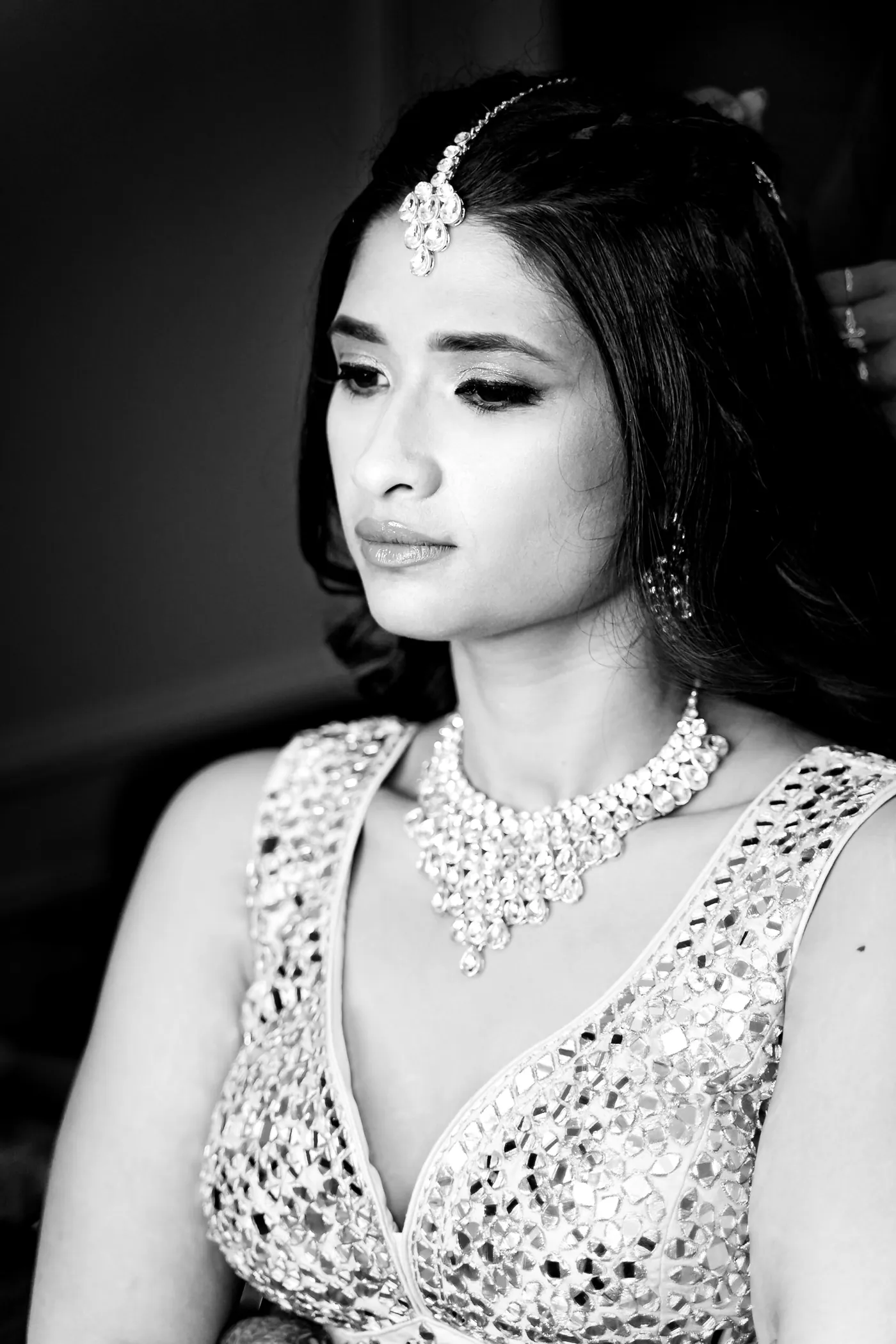 In black and white, Medha looks down in a mirror work blouse and a layered crystal necklace