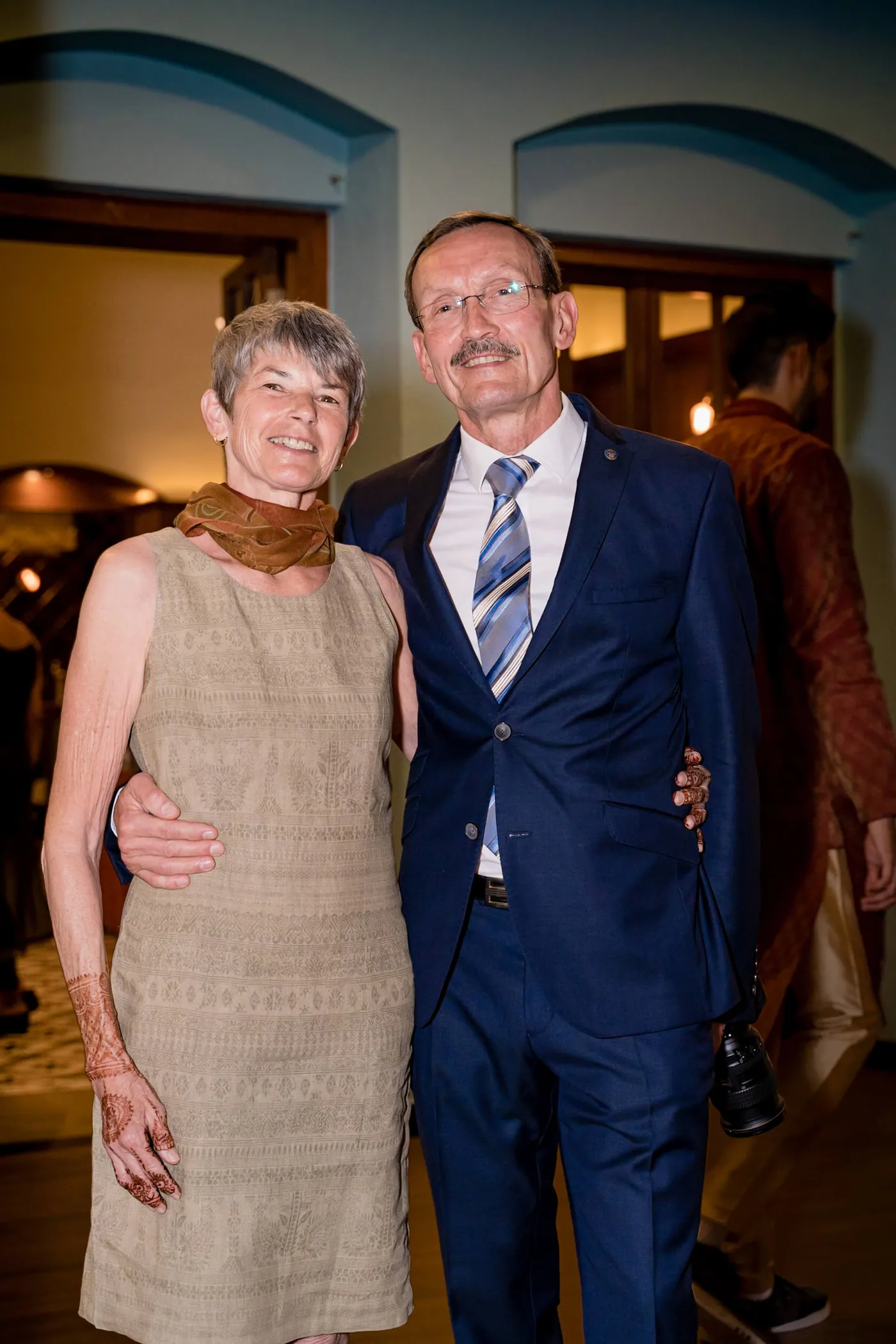 Stefan's parents pose arm in arm in front of a blue arched doorway at the club