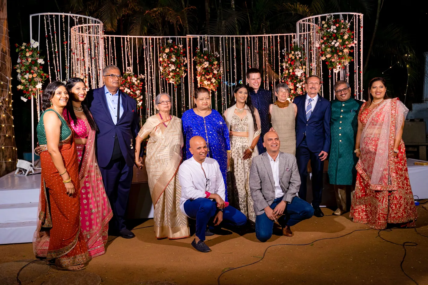 Family members stand and crouch in a row, some seated on the floor, in front of the lit backdrop