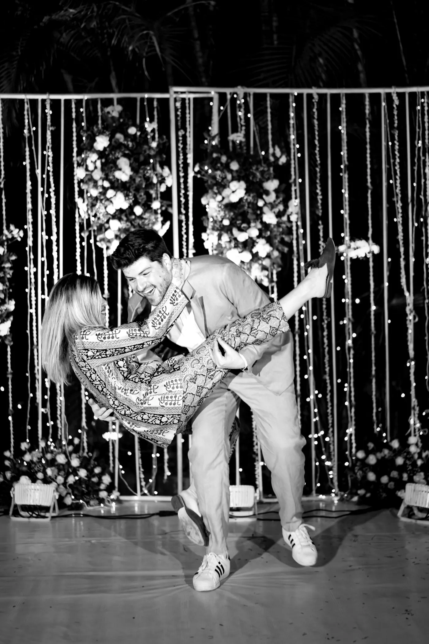 In black and white, a woman in a sparkling dress is dipped backward by a man before the backdrop
