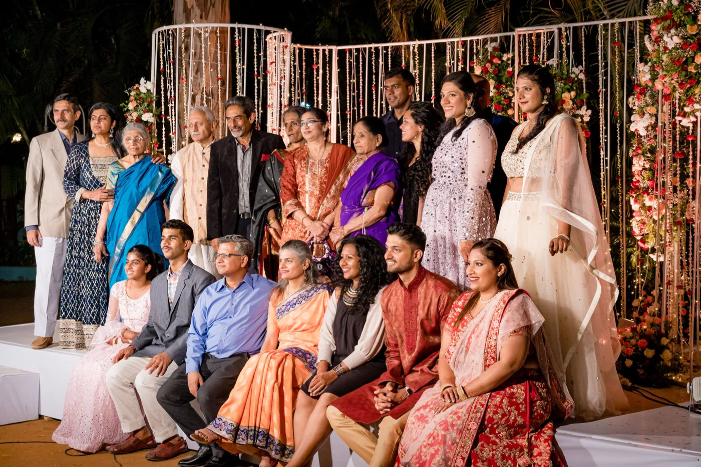 Family members sit in rows on the stage and others stand behind them for a large group portrait