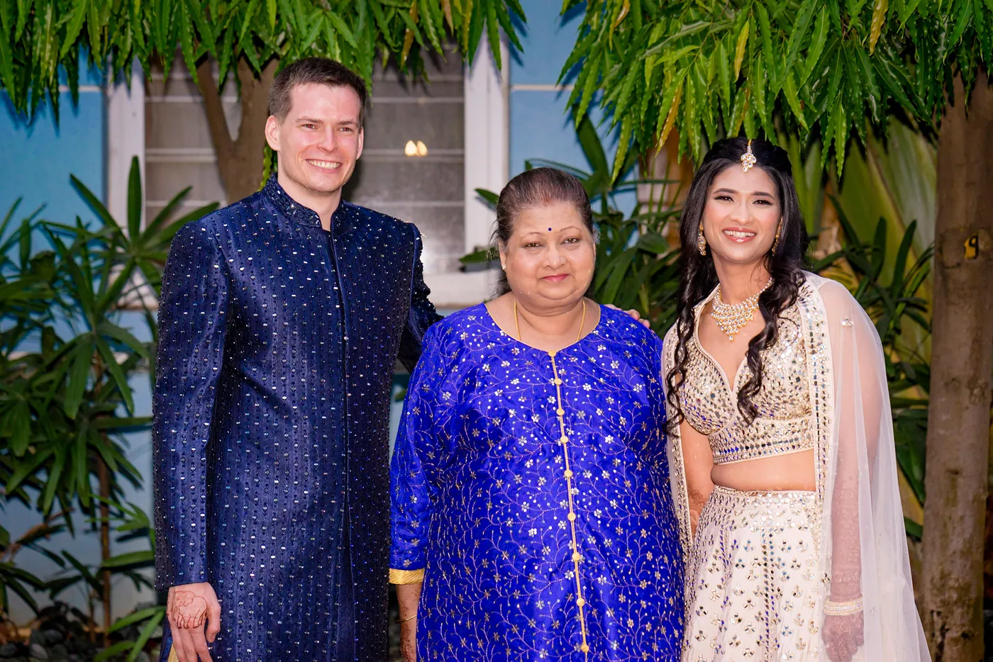 Stefan, a woman in a bright blue kurta and Medha pose together in front of green leaves