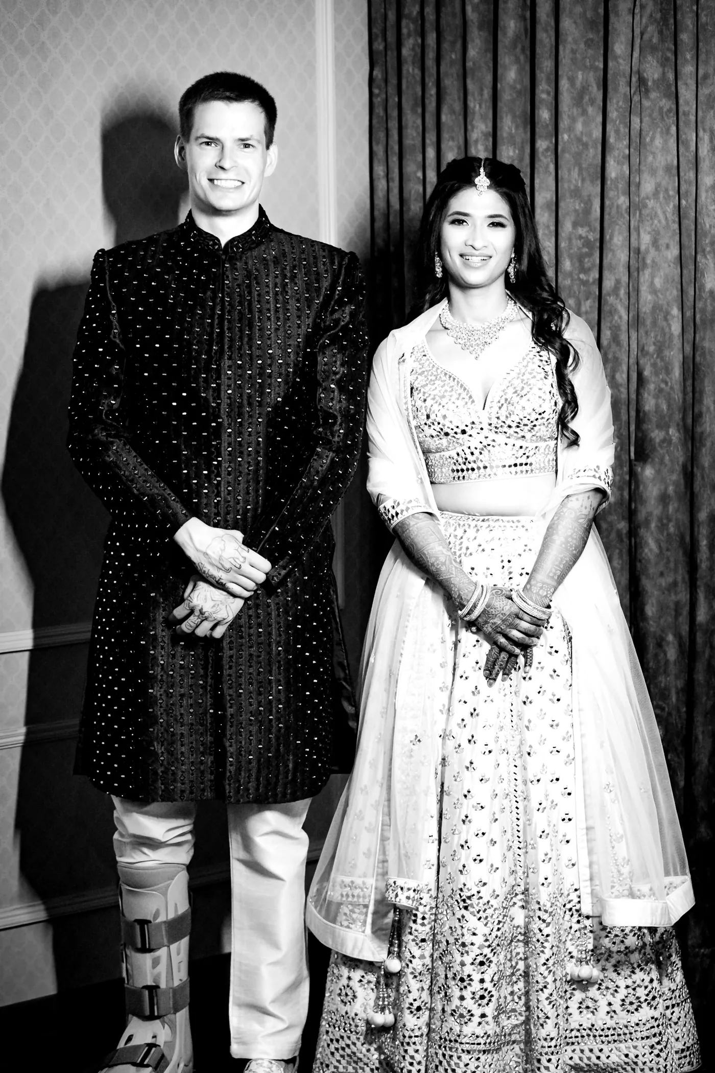 Stefan and Medha pose in front of wood panelling, and a medical boot is visible on Stefan's ankle