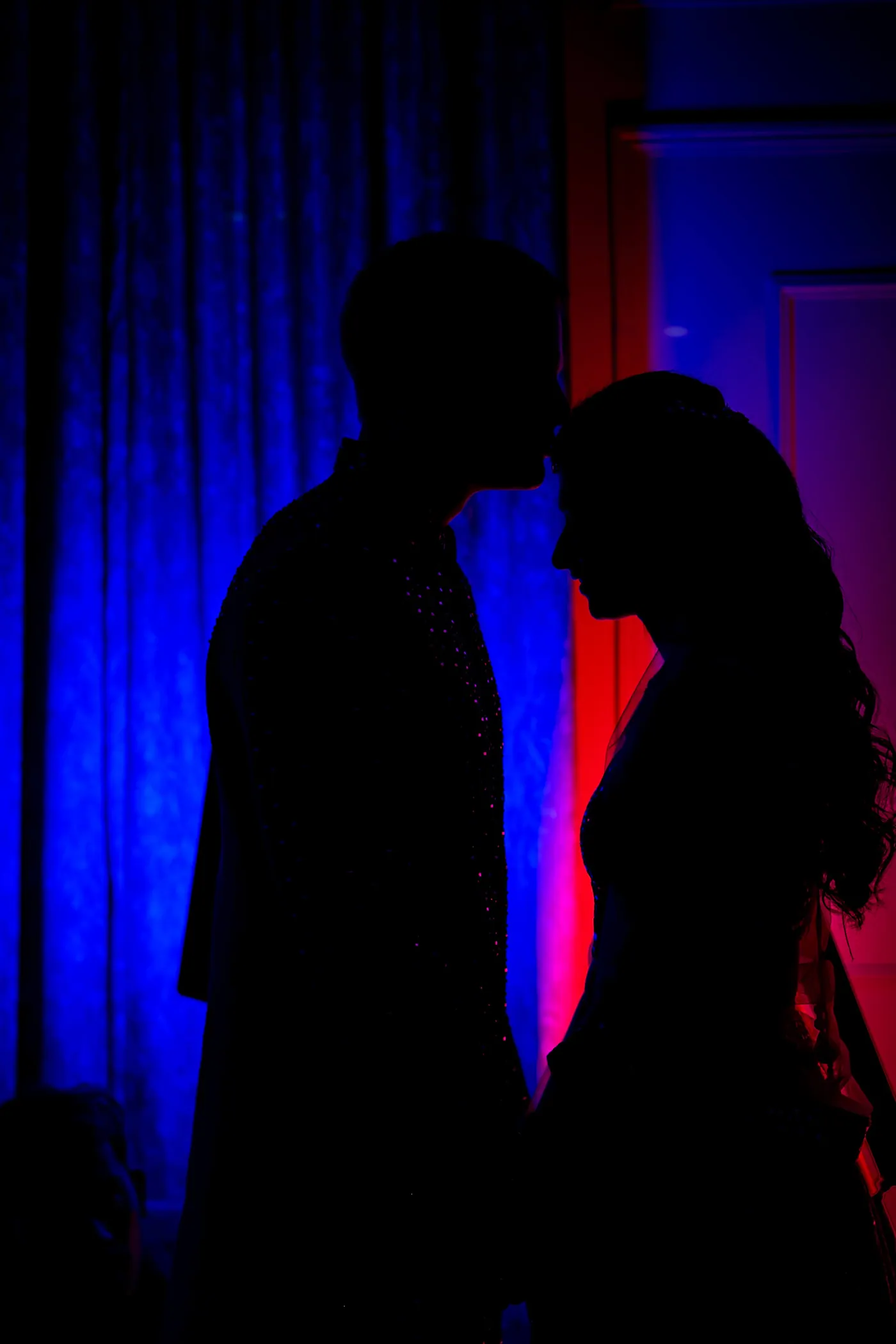 Blue and magenta light turns Stefan and Medha into silhouettes as they lean in close
