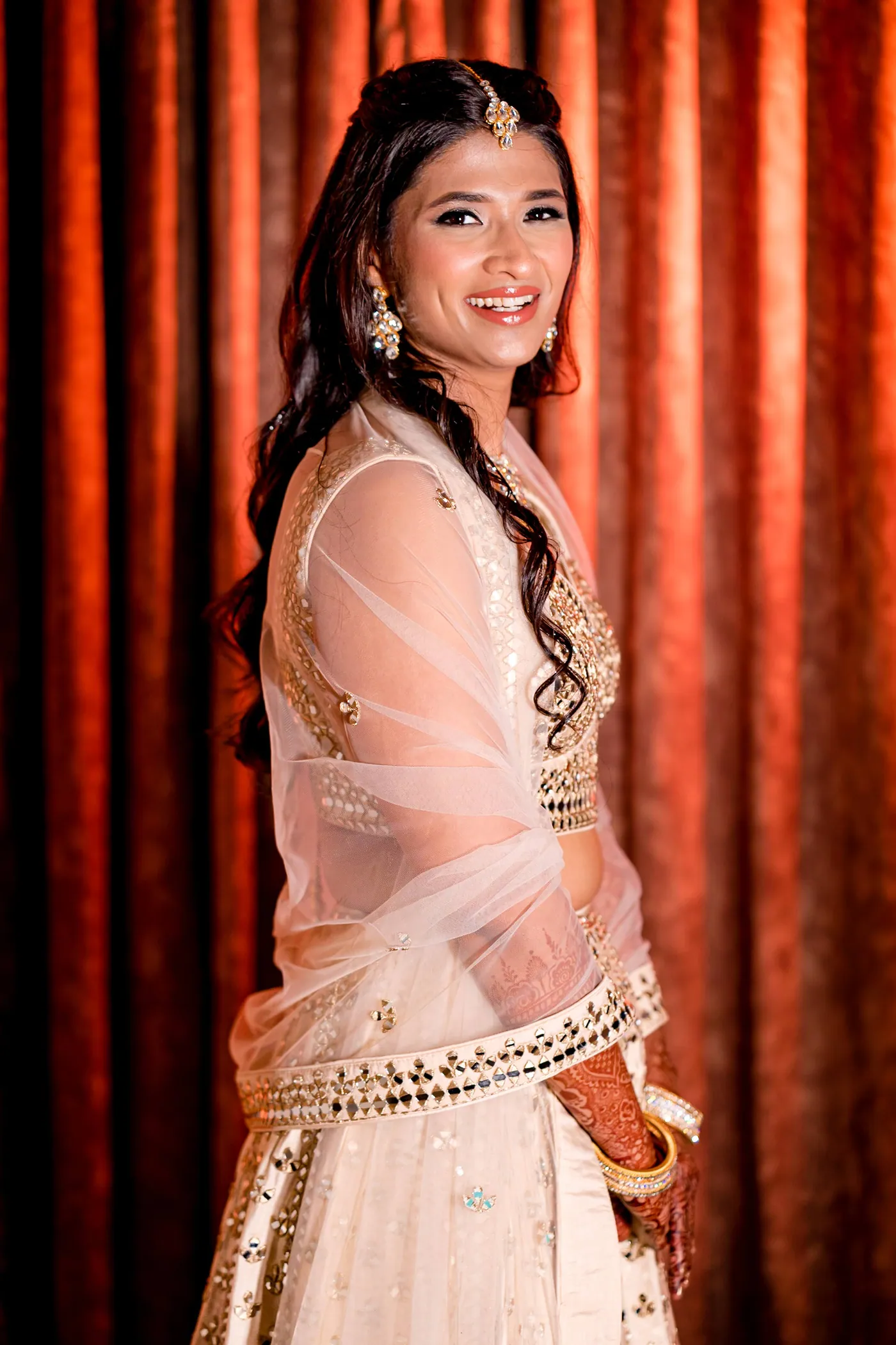 Medha laughs openly with her head turned, hair falling over a pale dupatta against rust curtains