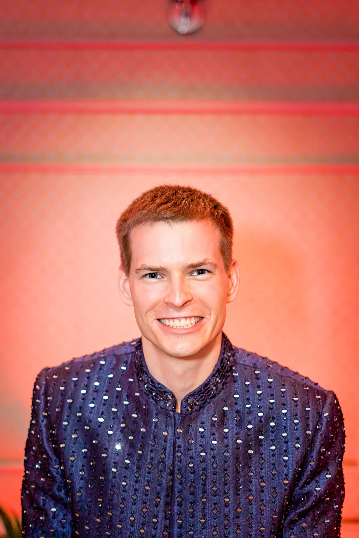Stefan grins widely at the camera in a navy sherwani sparkling with small sequins