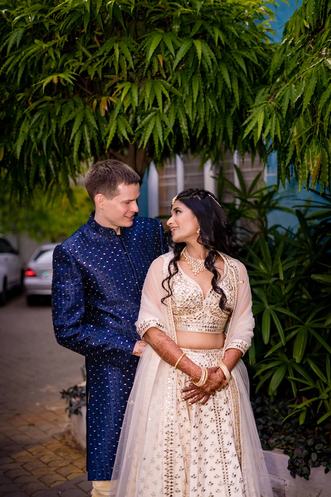 Stefan and Medha stand close together on the lawn with trees behind them