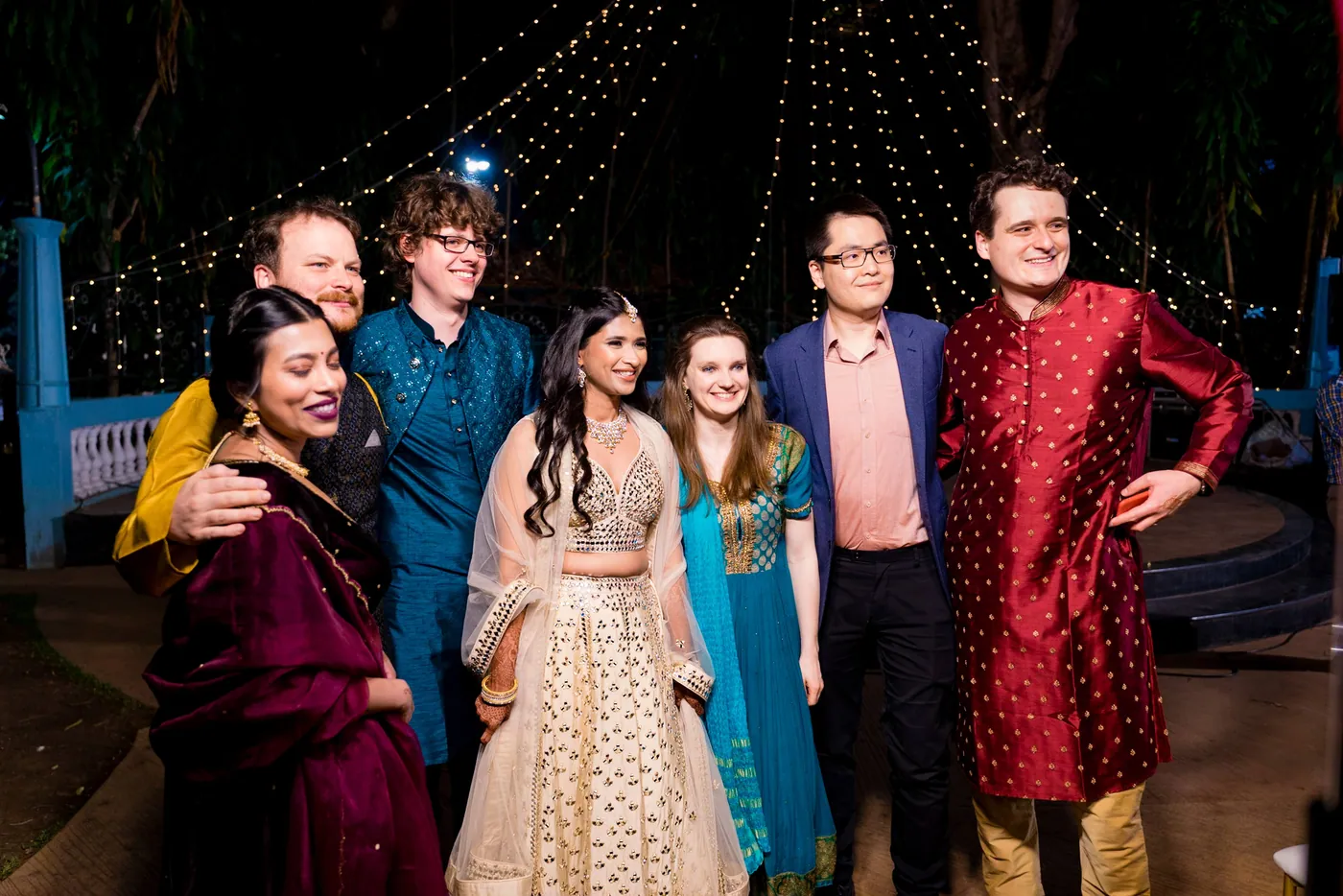 Seven friends in saturated lehengas and kurtas pose together on the dance floor