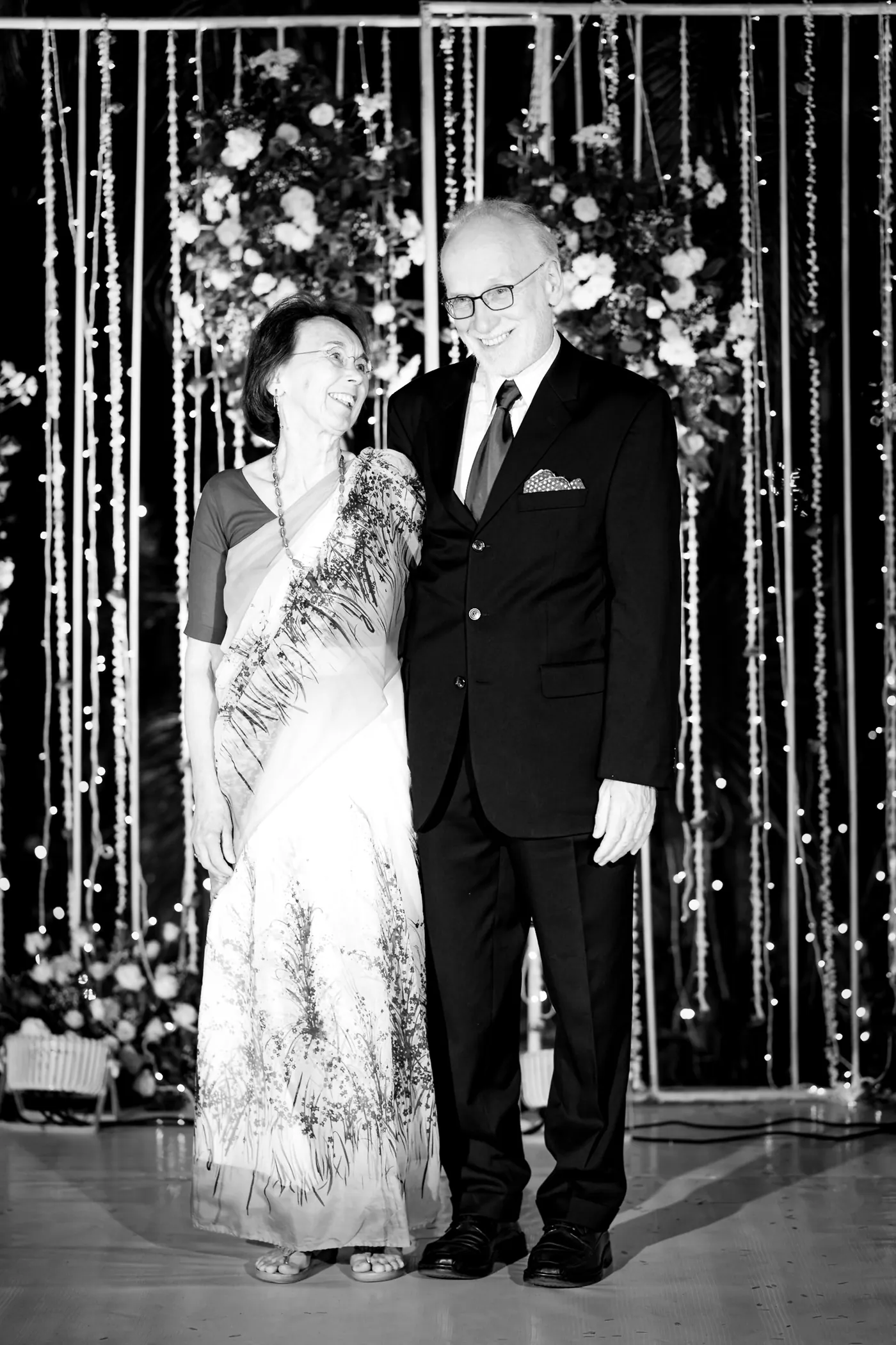 In black and white, a man in a dark suit and a woman in a pale sari stand together