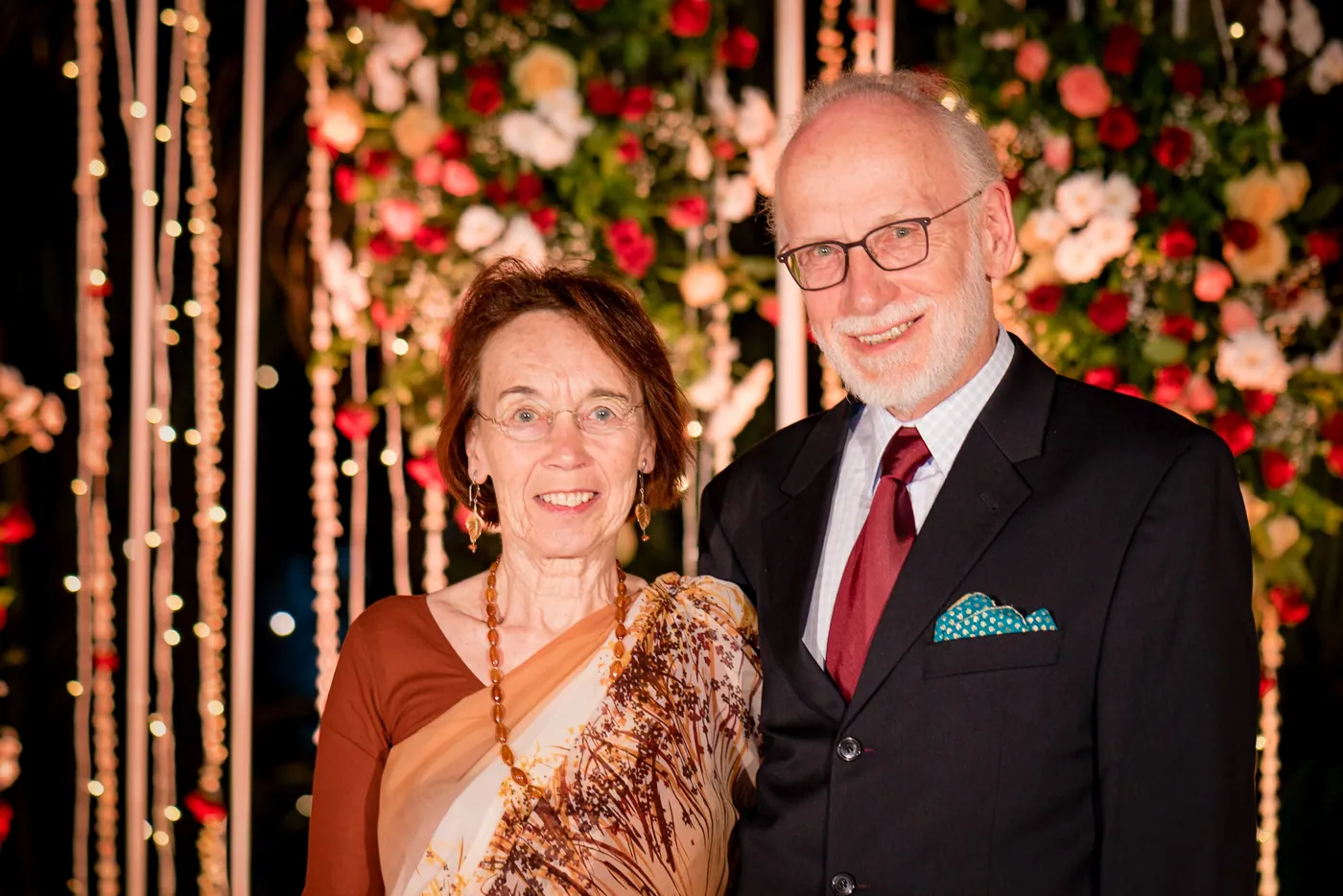 Stefan's grandparents stand together in front of the flower arrangements at The Bangalore Club