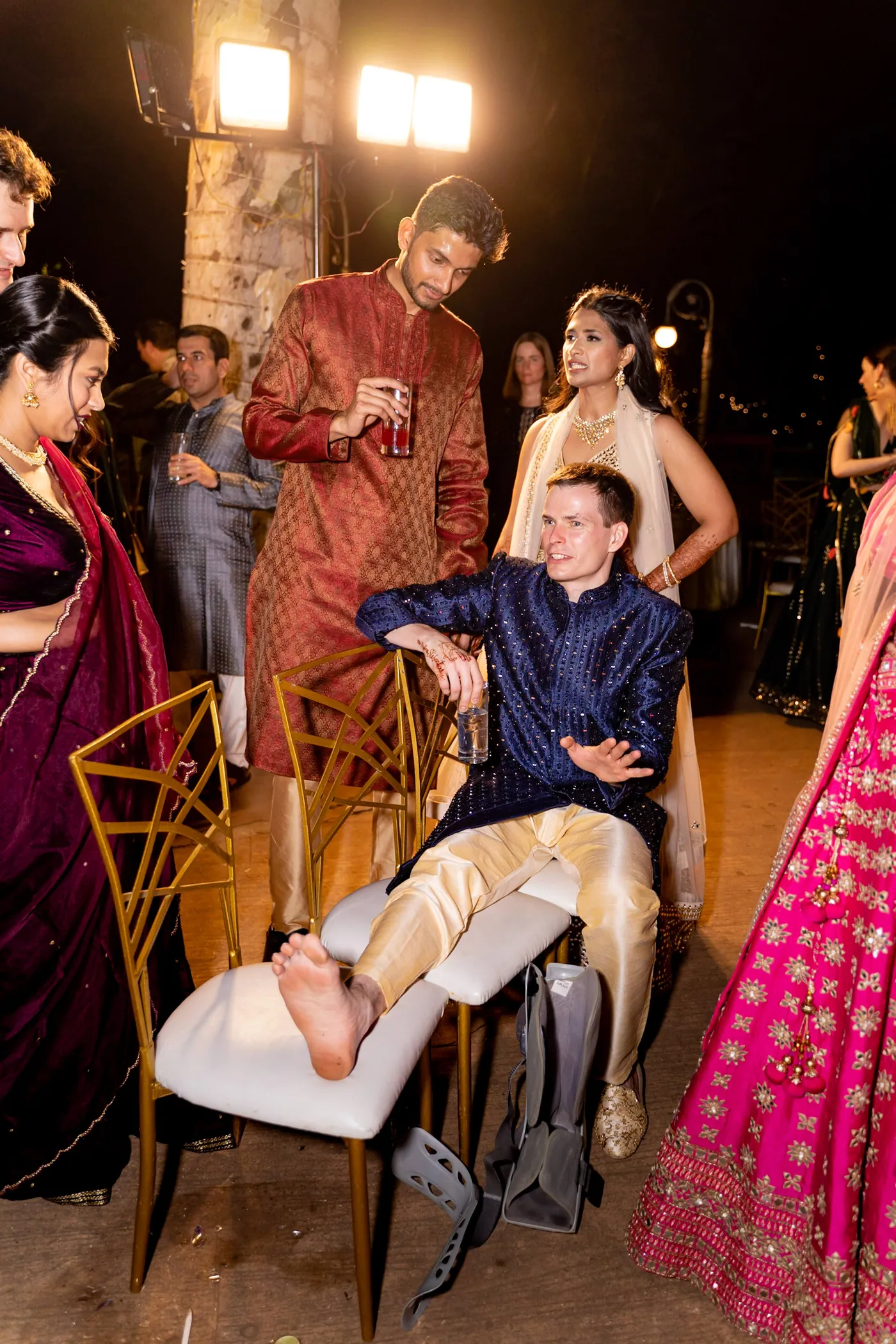 Stefan sits sideways on a gold chair with his leg propped on another, a medical boot on his ankle