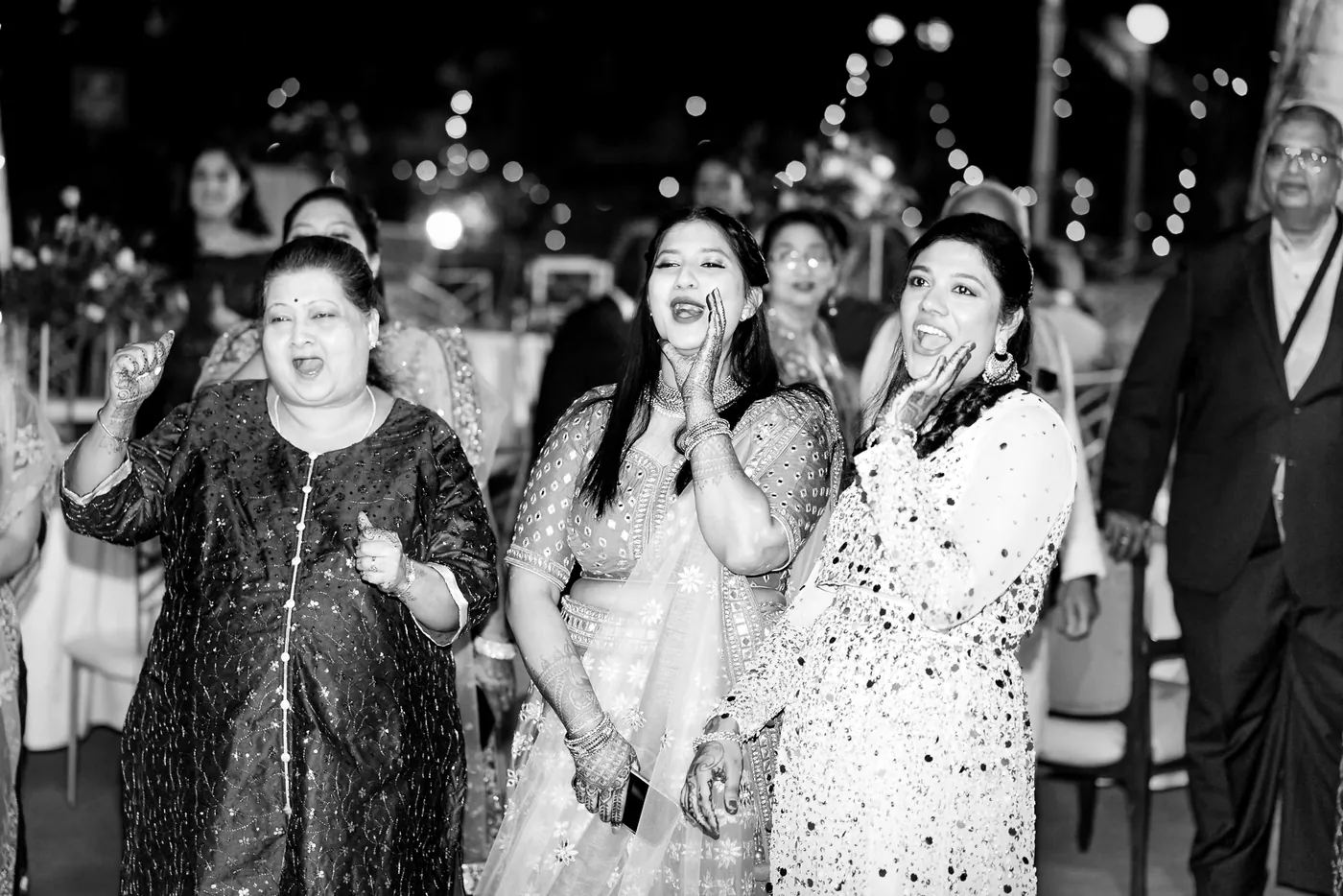 In black and white, women laugh and dance close to the camera while a man looks on