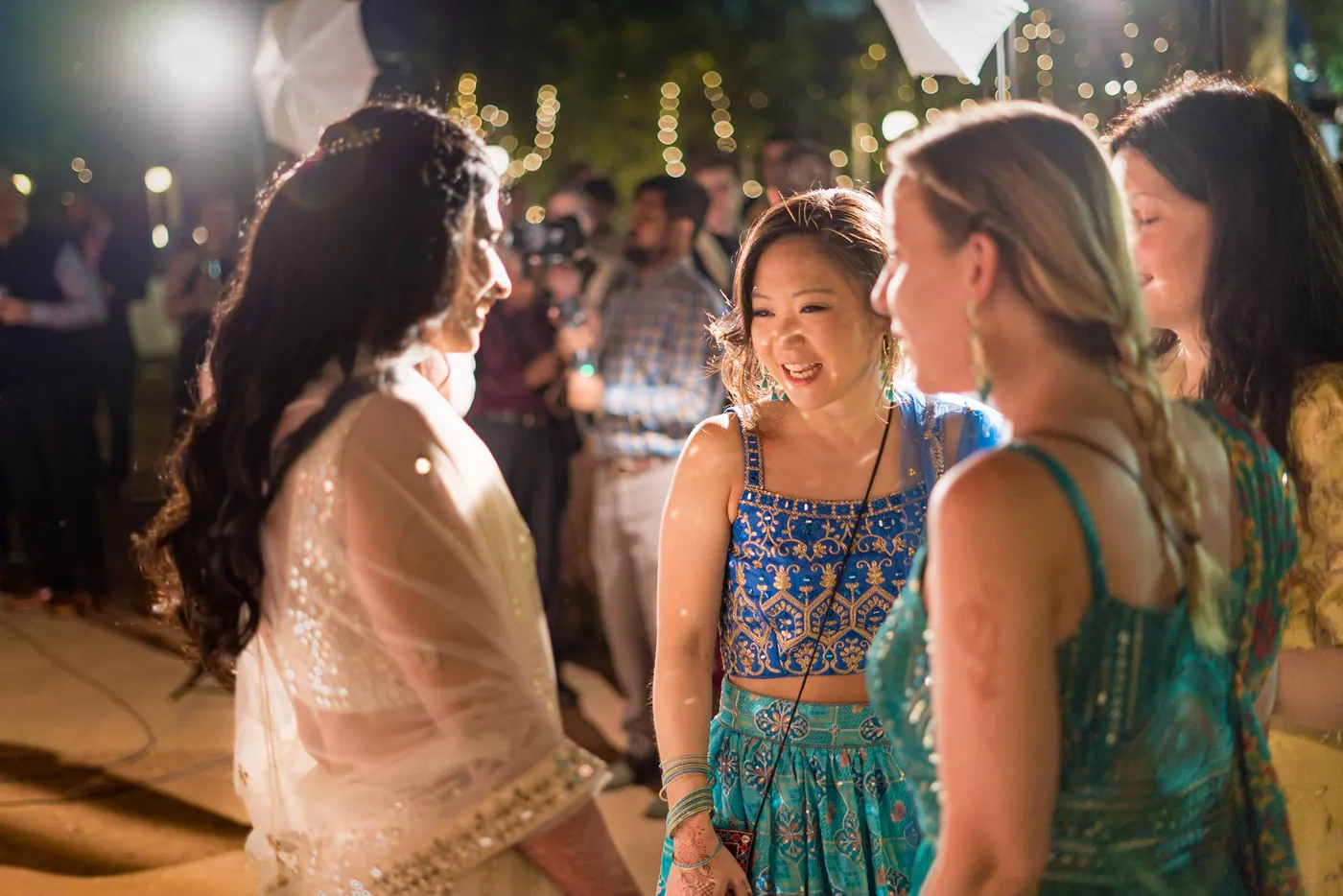 Two women laugh together beside a woman in a blue crop top in the glow of the party lights