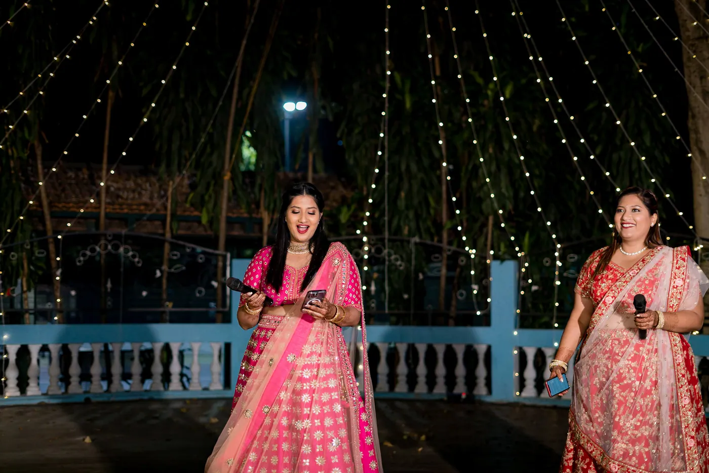 Two women in pink lehengas stand on the dance floor with the lights strung above them