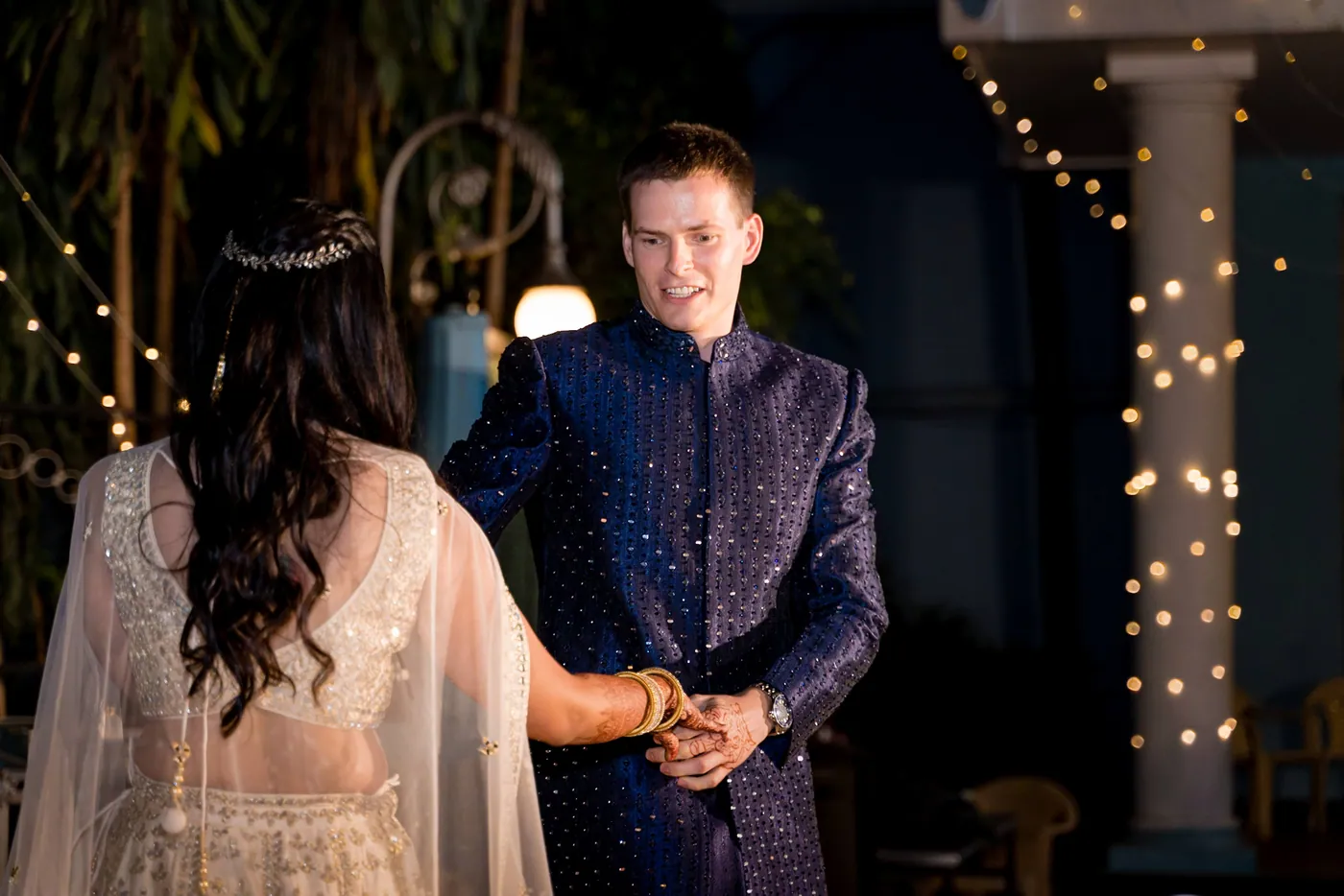 Medha and Stefan hold hands face to face on the dance floor with the club building glowing behind them