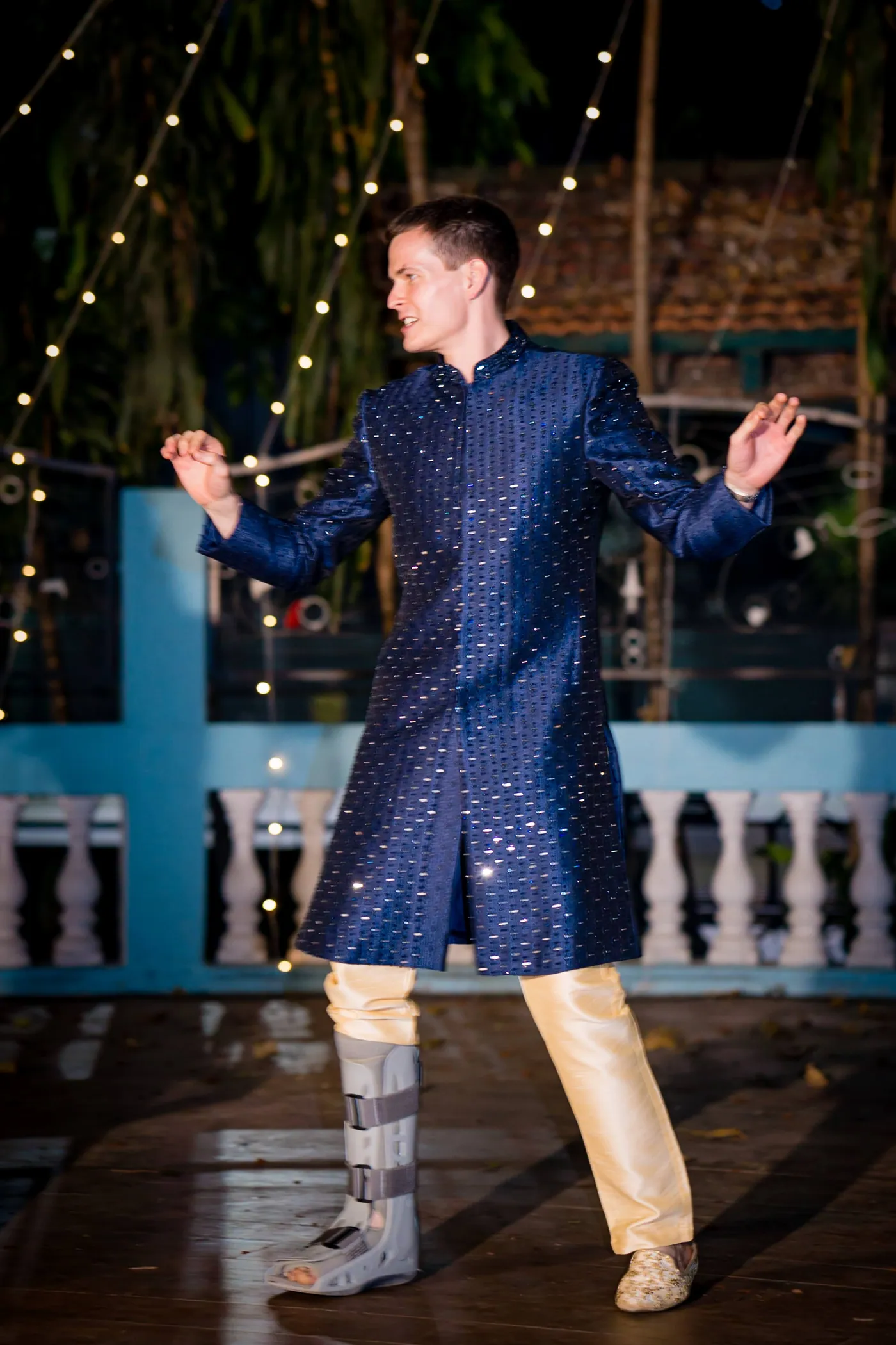 Stefan dances solo in a navy sherwani with his arms out and a medical boot on one leg