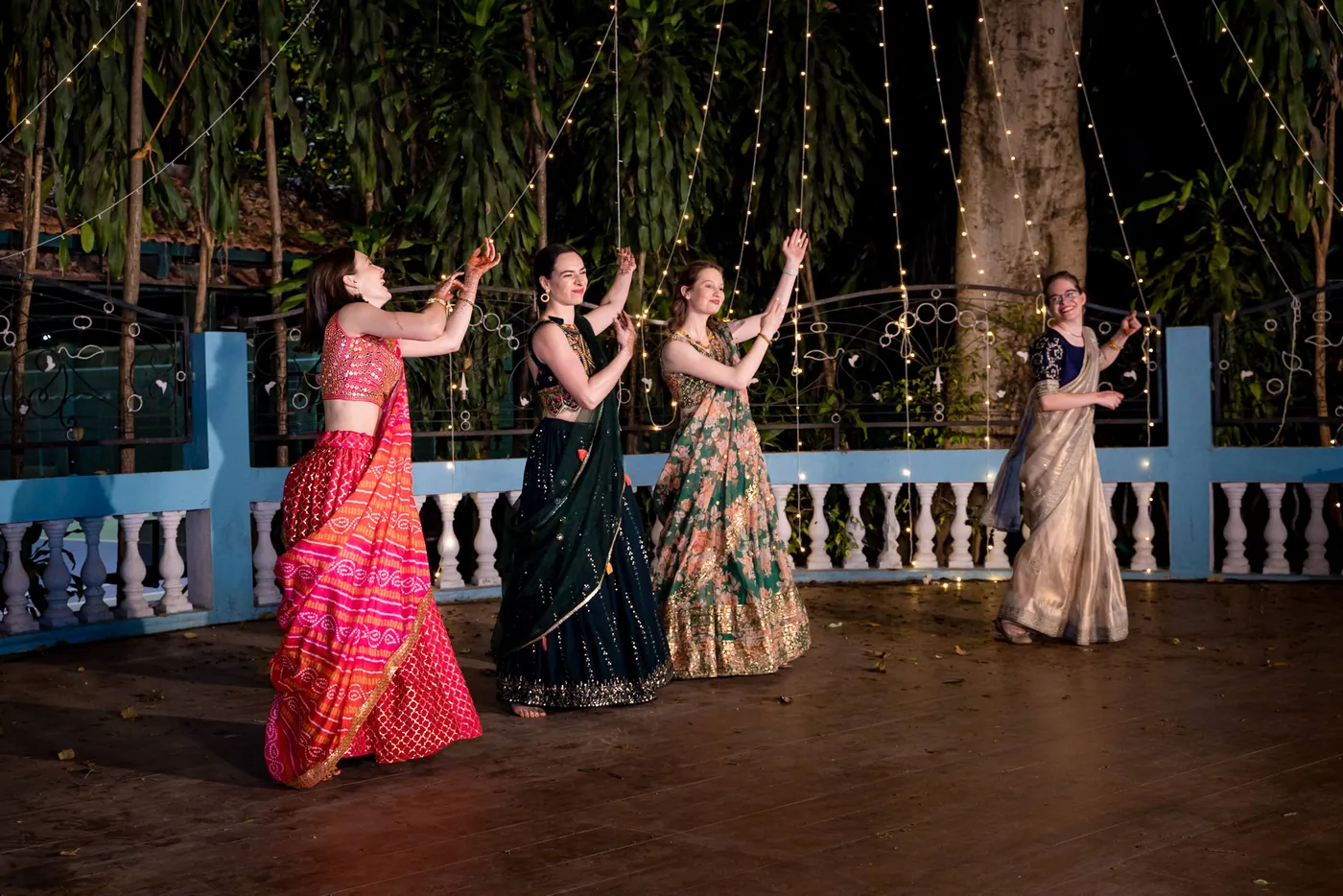 Women in pink, green and cream lehengas dance in a row with their arms up