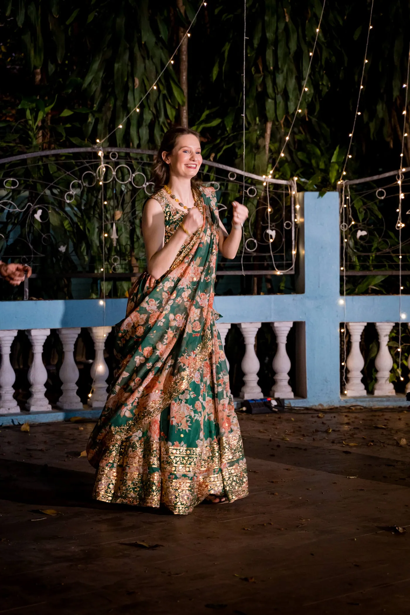 A woman in a green and orange lehenga saree dances alone with a smile