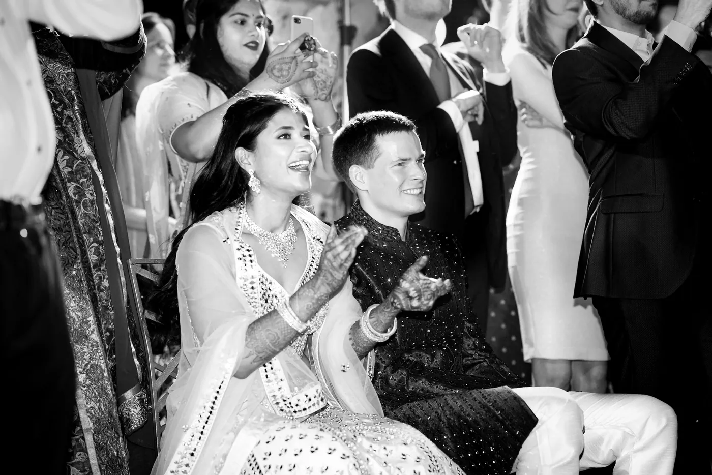 In black and white, Medha claps beside Stefan while the crowd presses in around them