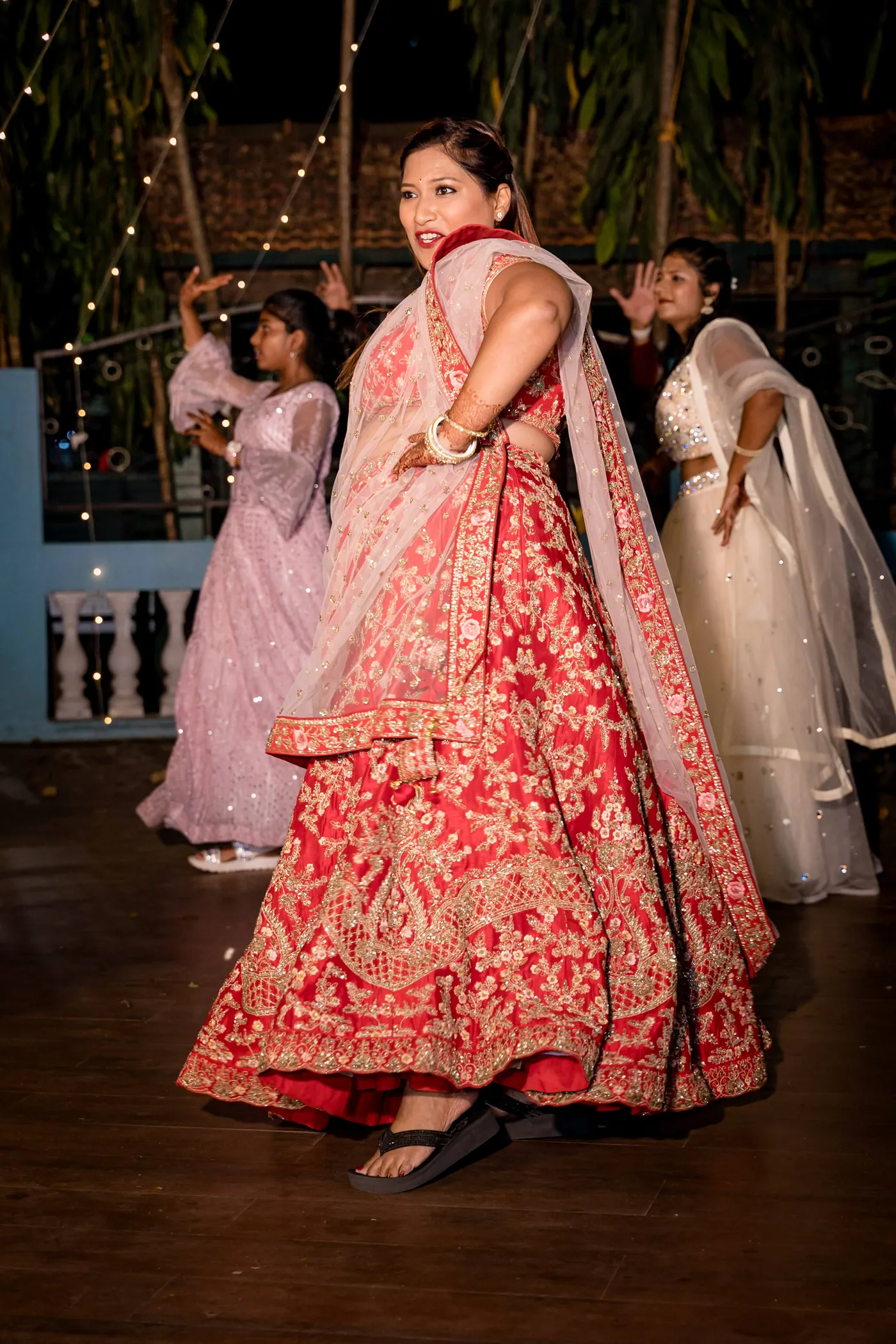 A woman in a red and gold lehenga twirls and looks over her shoulder