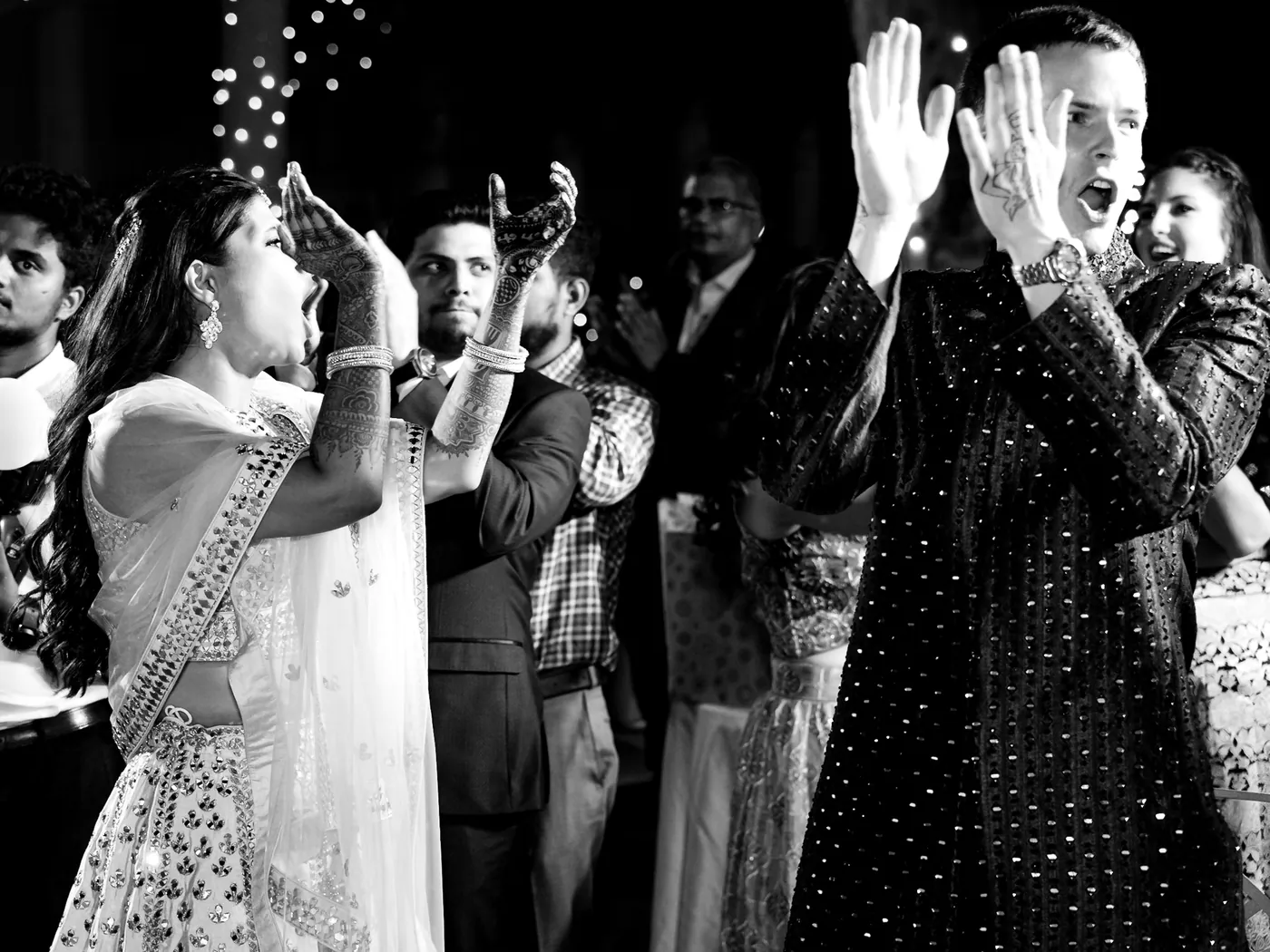 In black and white, Medha cheers and raises her hands as a crowd claps around her