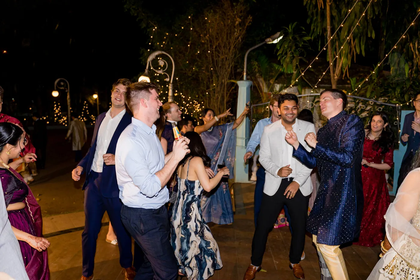 Stefan and other men in shirts and kurtas dance on the floor as lights glow behind them