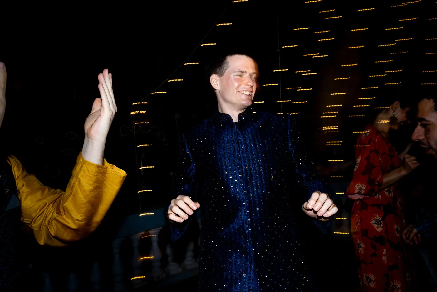 Stefan smiles and shimmies in a motion streaked frame beside a woman in a yellow sleeve
