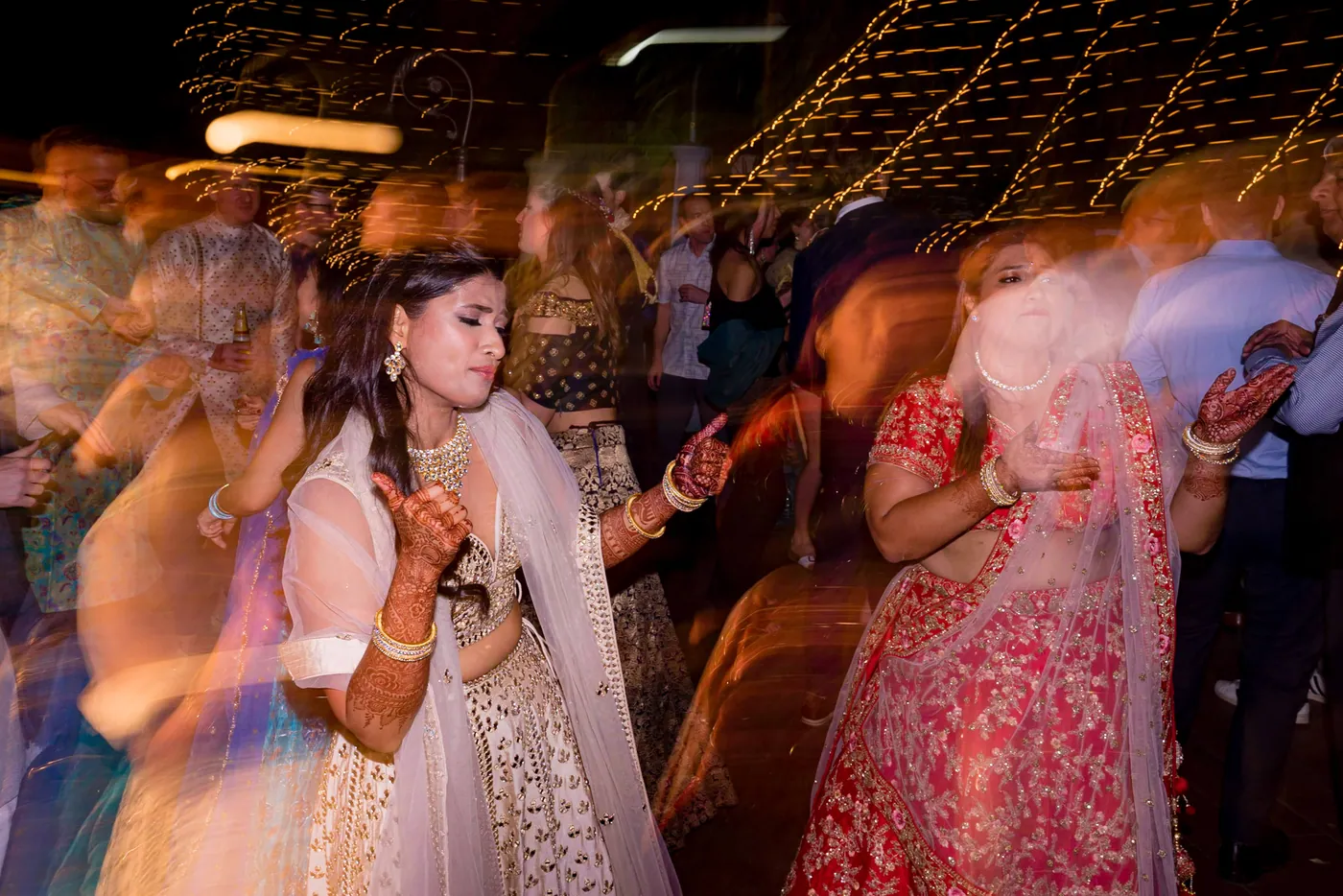 A slow shutter blurs Medha and her sisters dancing in pink and cream as lights streak behind them