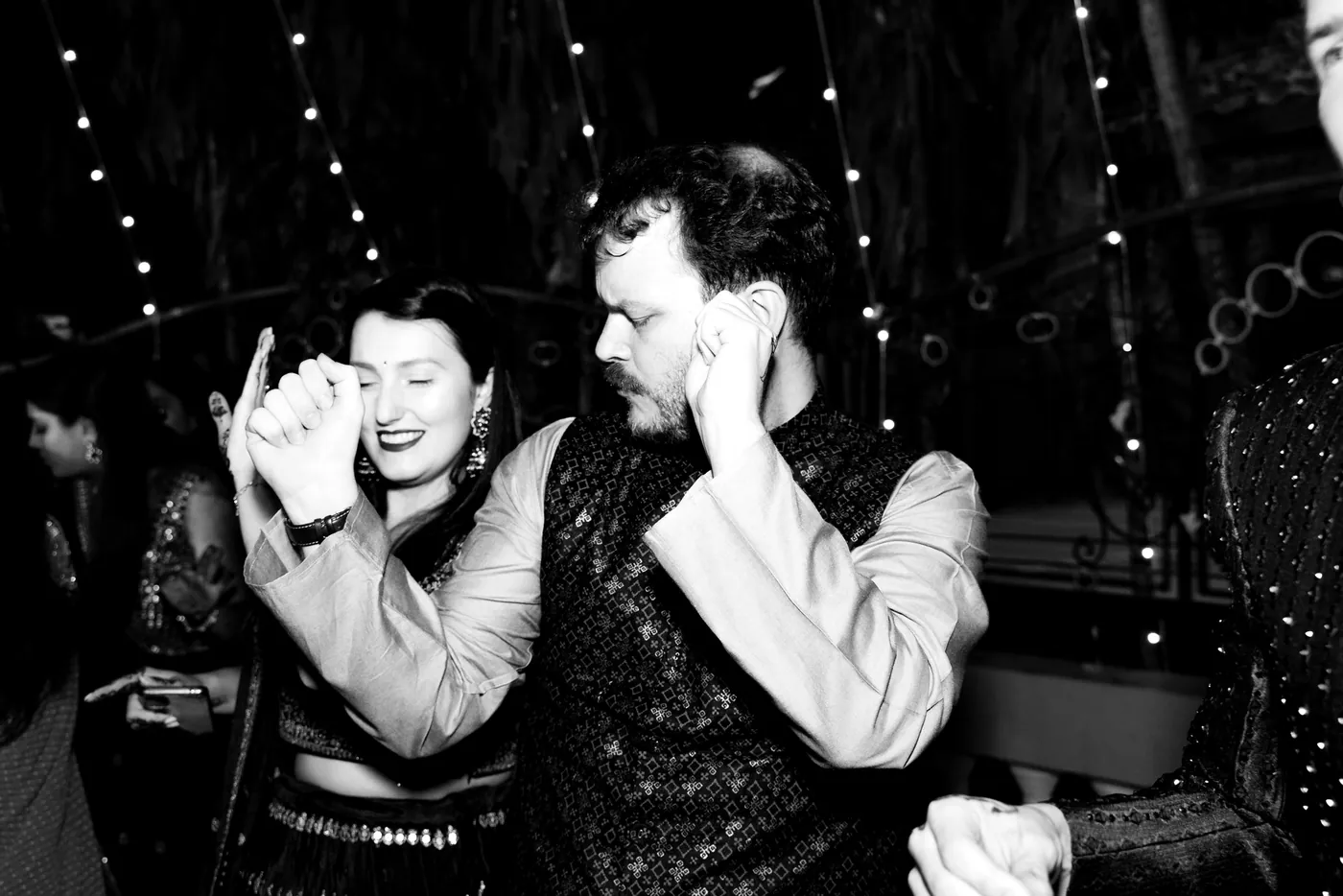 In black and white, a man in a waistcoat and a woman in dark dress laugh while dancing