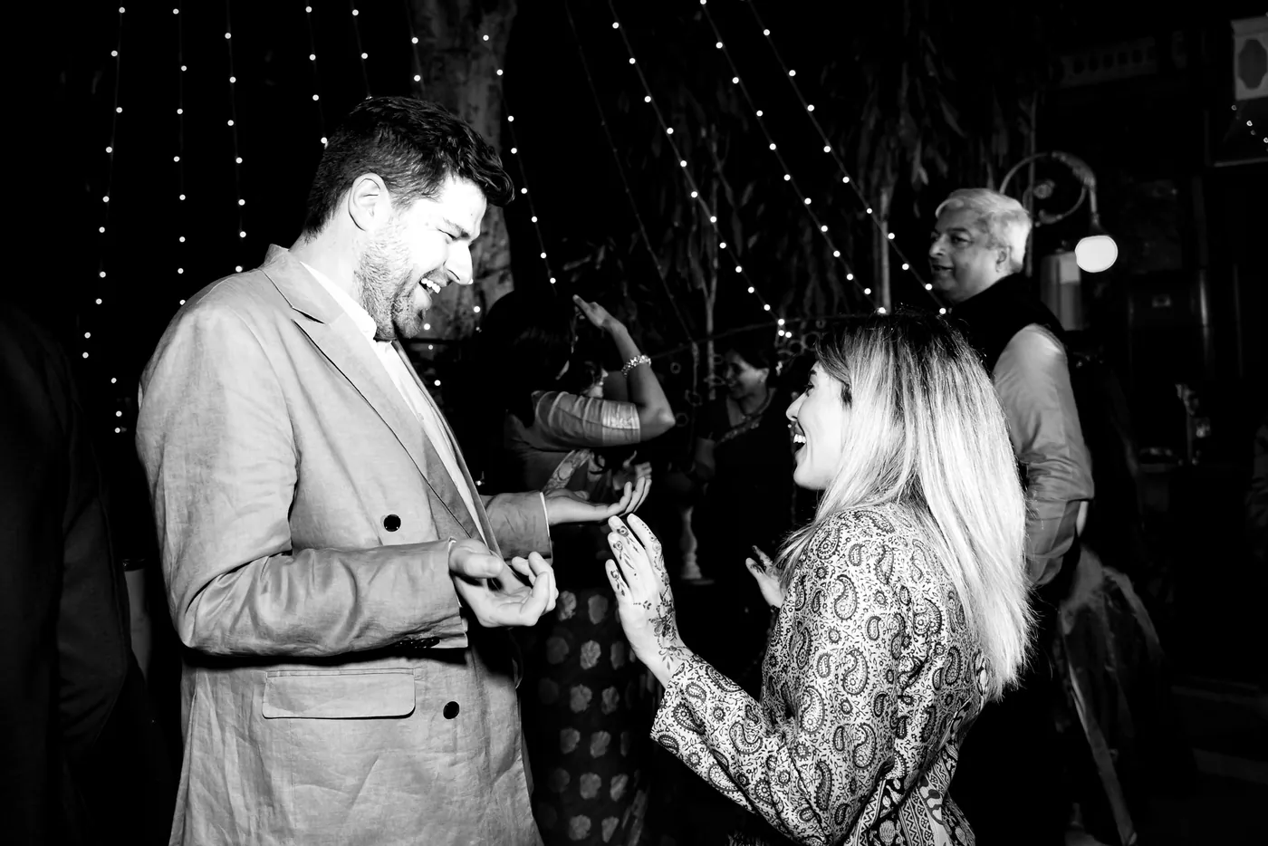 In black and white, a man in a jacket and a blonde woman share a dancing moment up close
