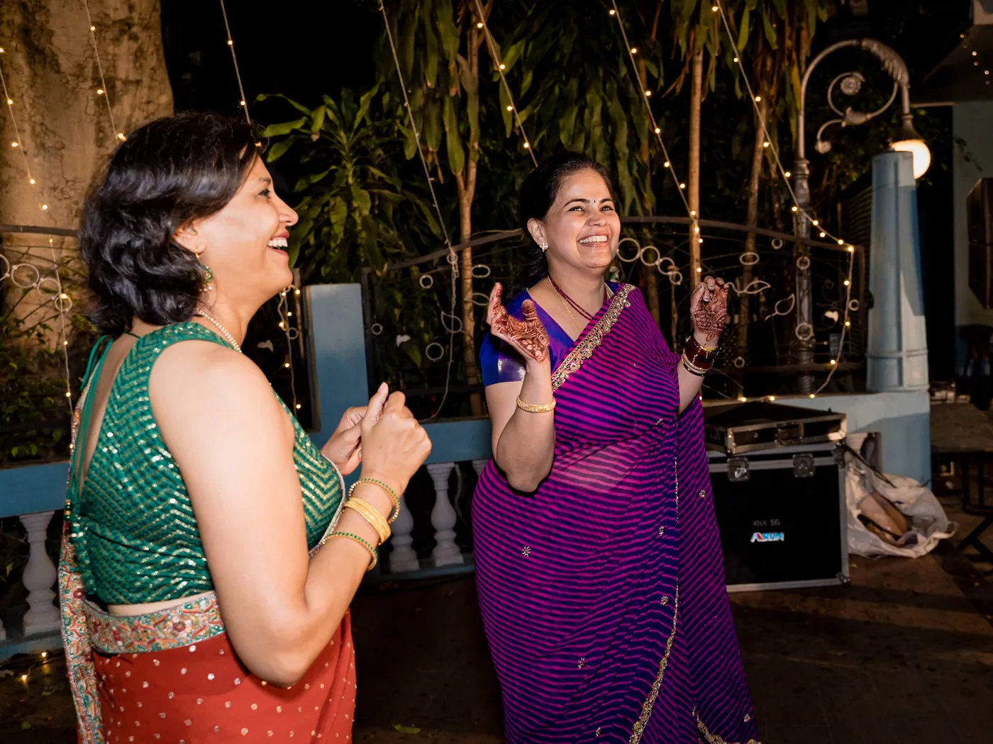 A woman in a green blouse and a woman in a violet sari laugh and dance