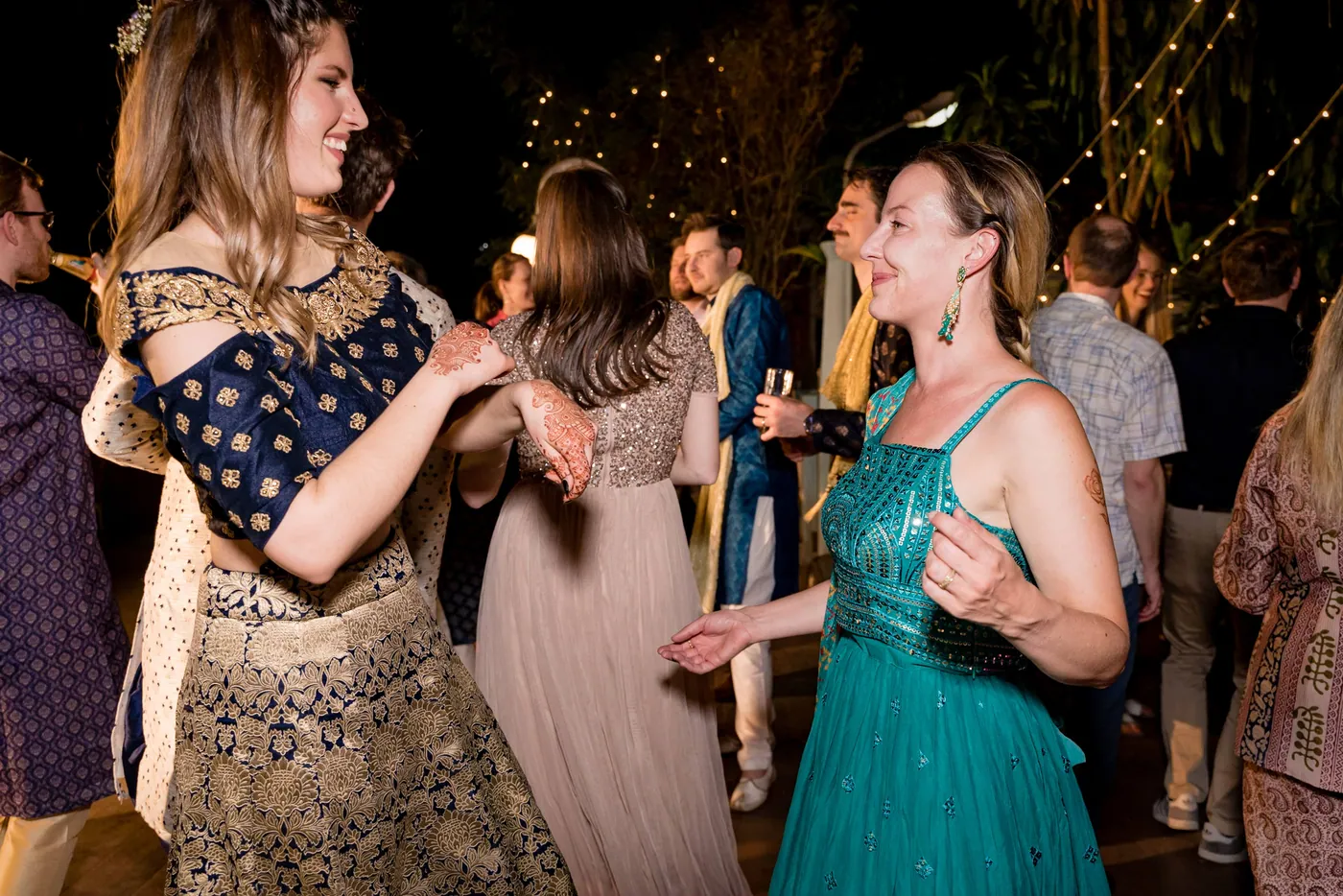 Women in a teal gown, a cream outfit and a dark dress dance with hands raised