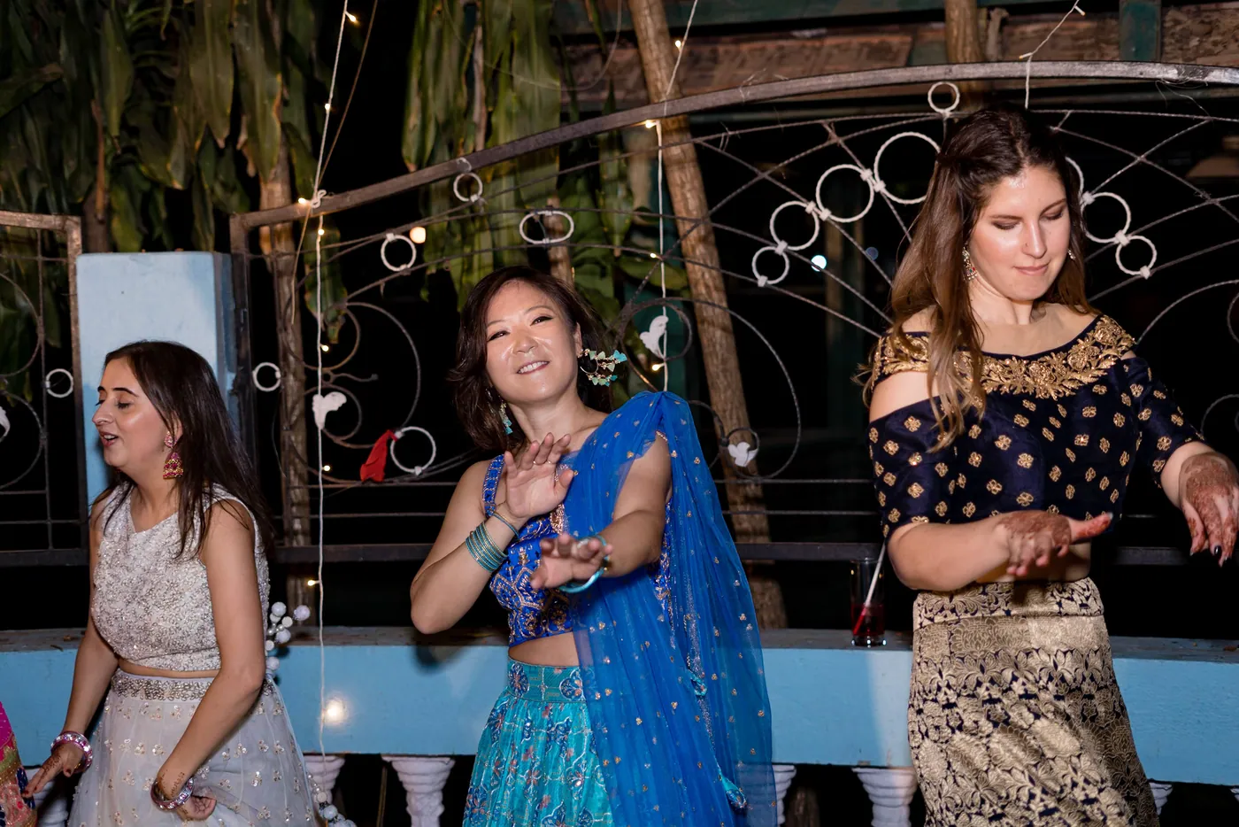 Three women in cream, blue and gold lehengas dance side by side