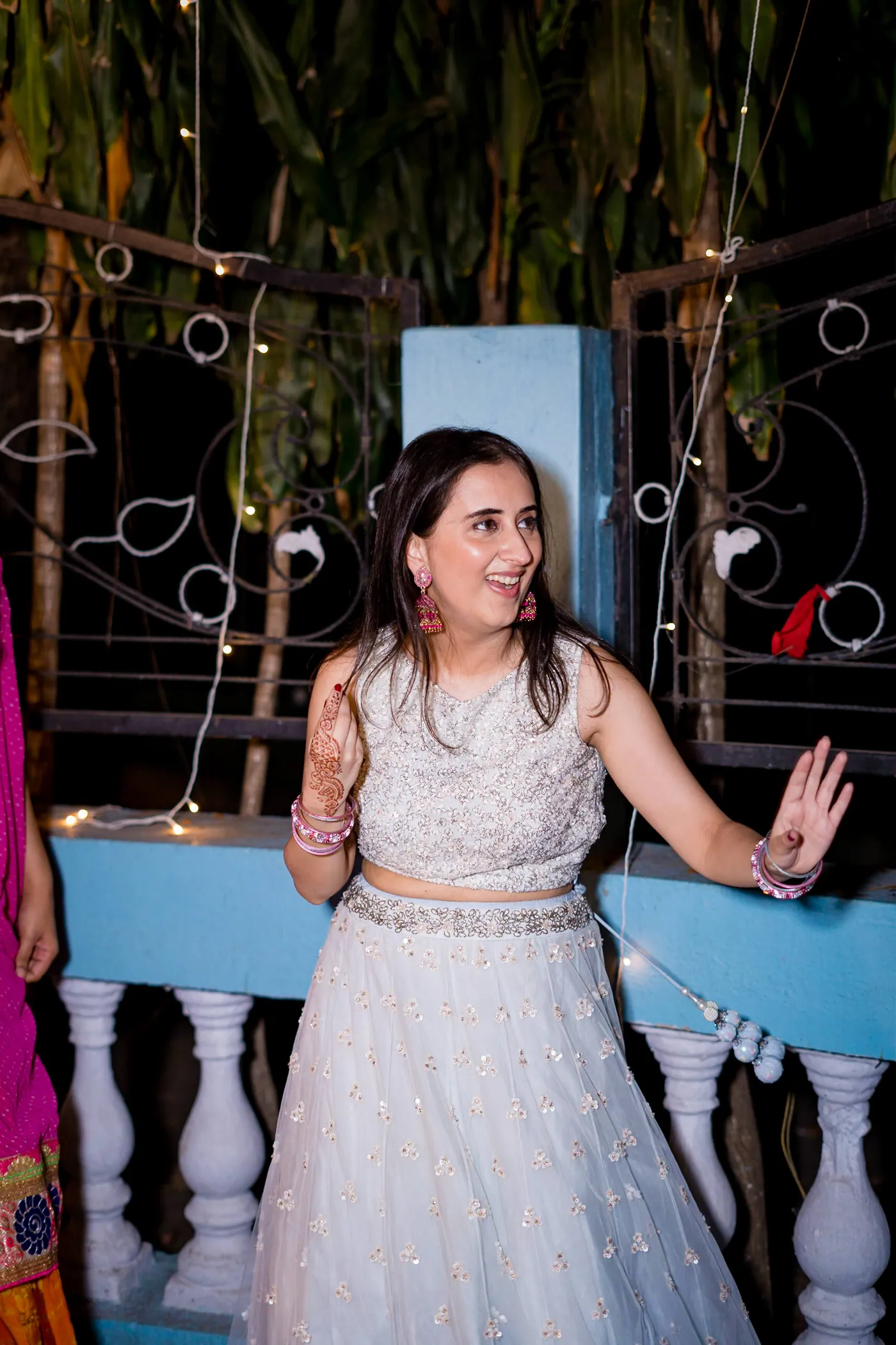 A woman in a white lehenga dances alone with her hand lifted