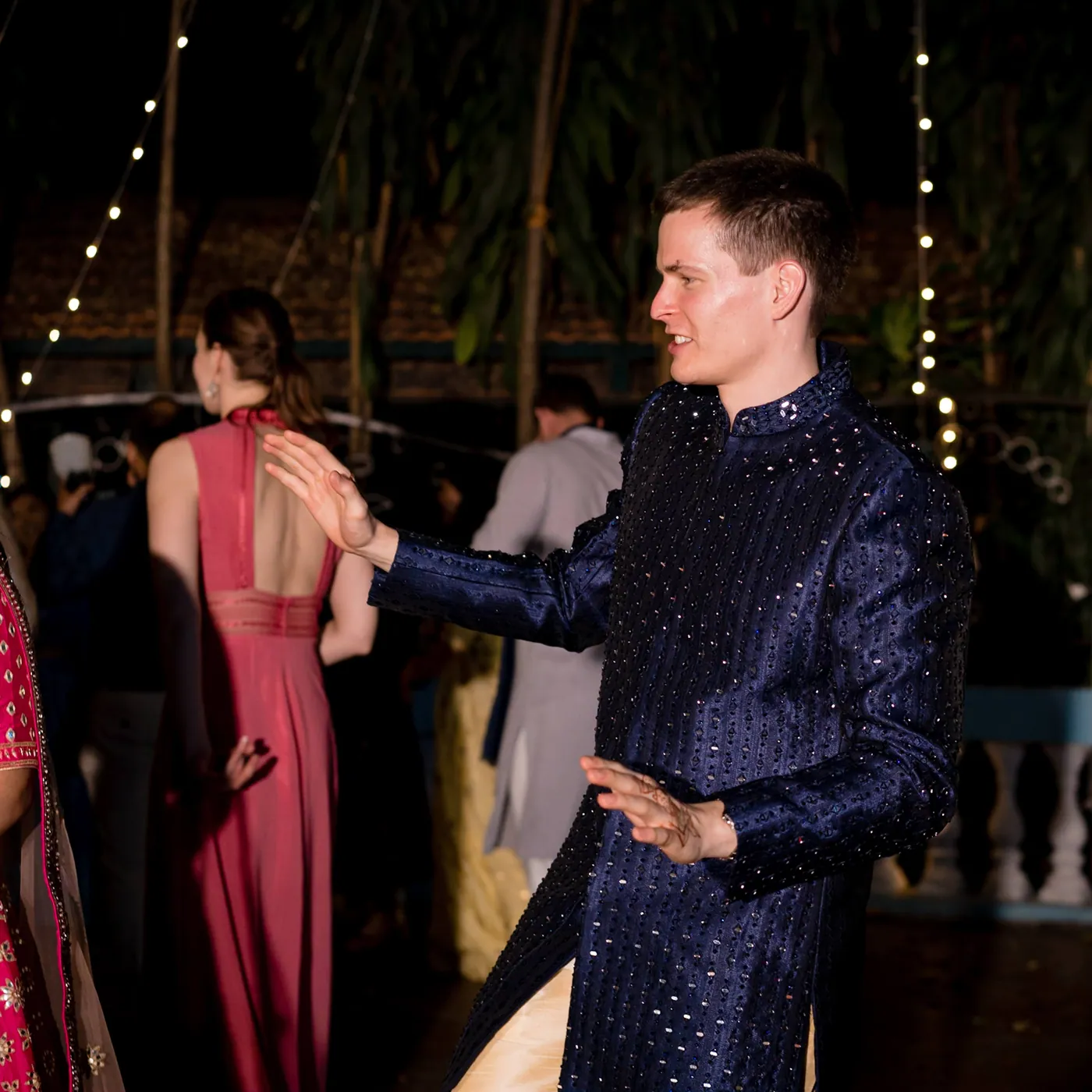 Stefan in navy dances in profile as a woman in a coral dress stands behind him