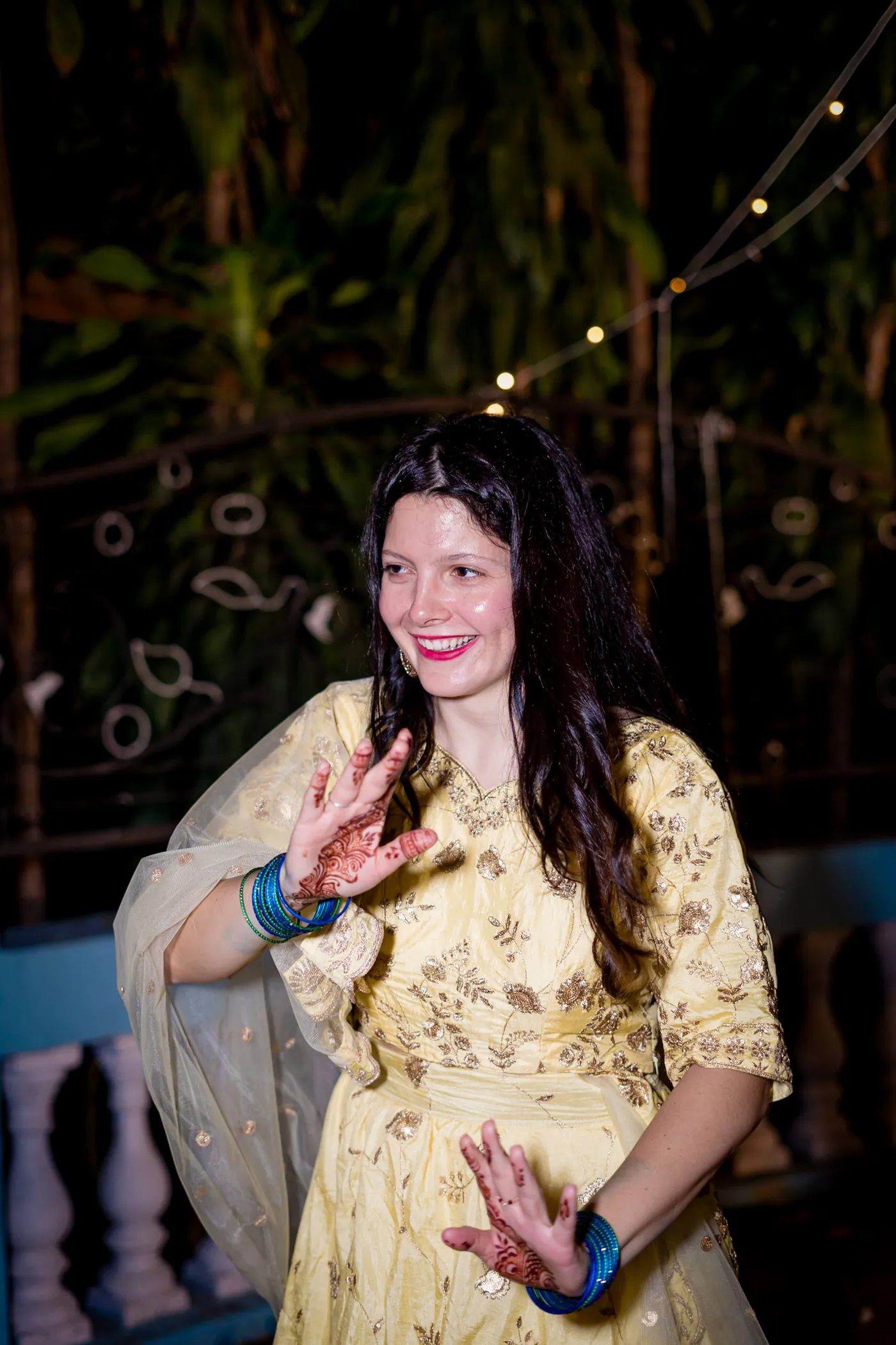 A woman in a pale yellow suit dances with a big smile and her hands cupped
