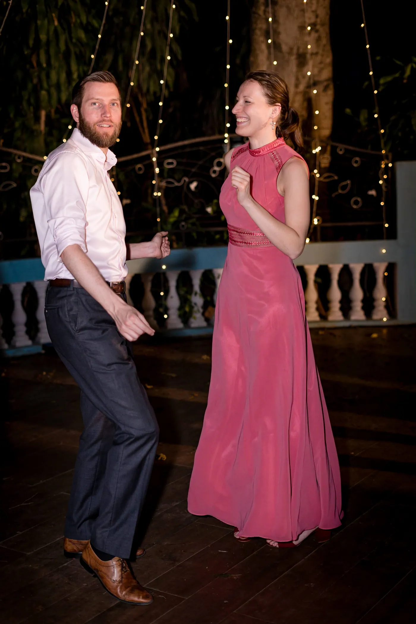 A man in a white shirt and a woman in a dusty pink dress dance together