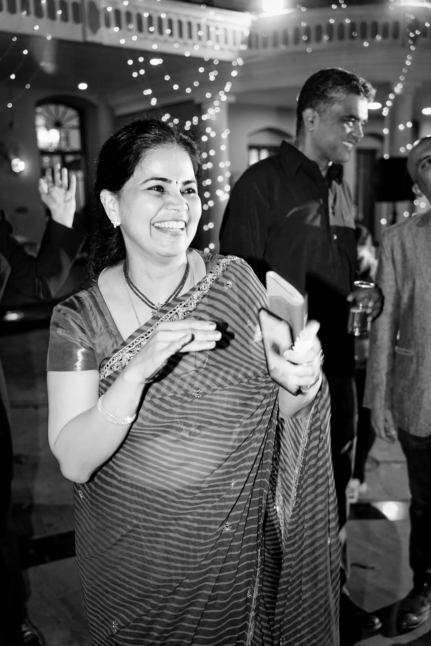 In black and white, a woman in a sari smiles in profile as she dances