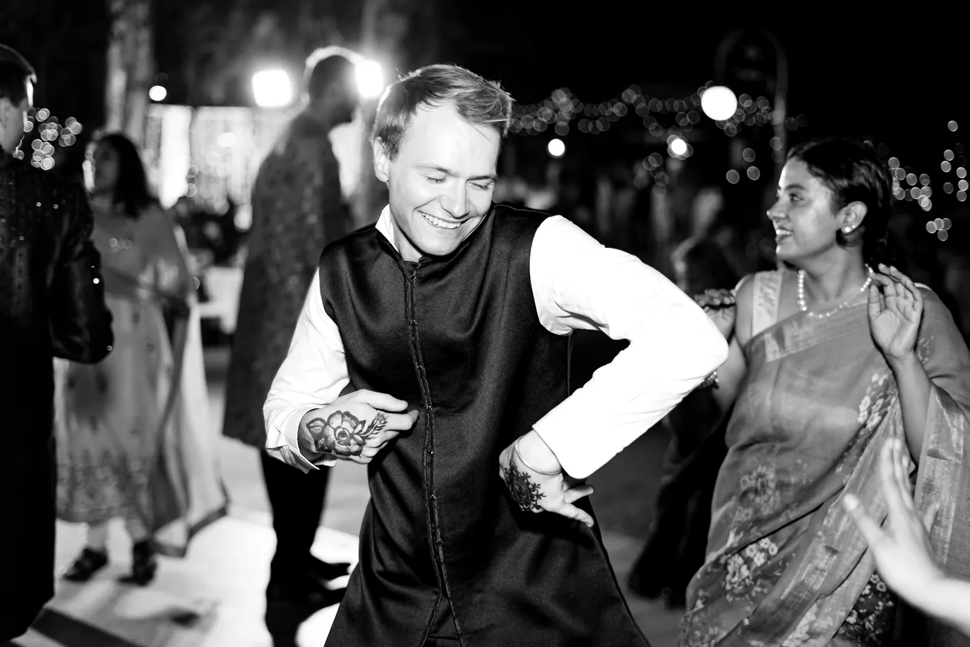 In black and white, a blonde man in a waistcoat dances with a hand raised