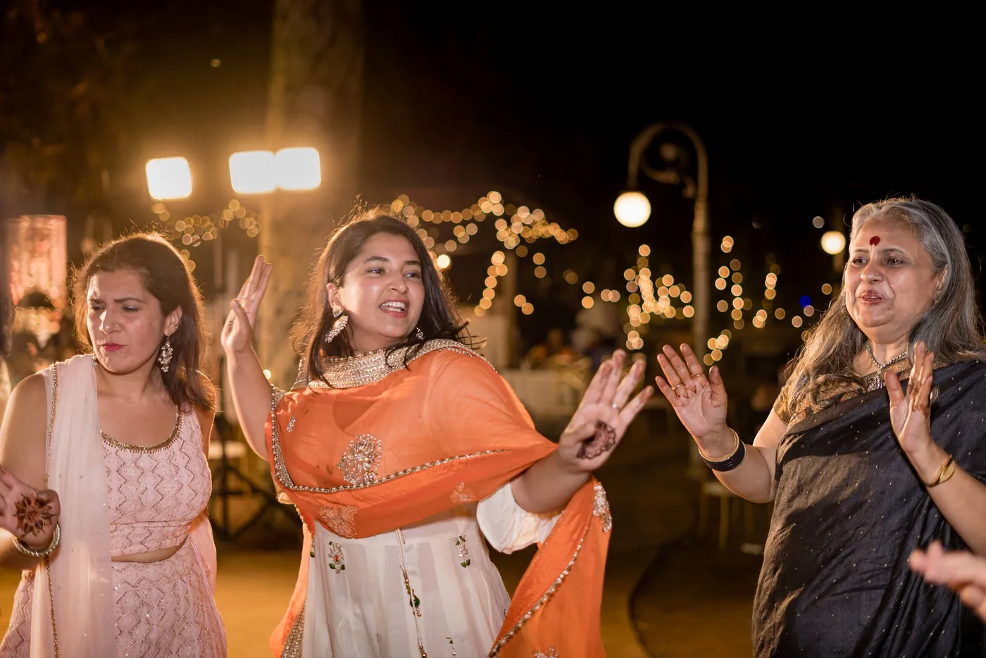A woman in an orange dupatta and a woman in a patterned sari dance beside each other