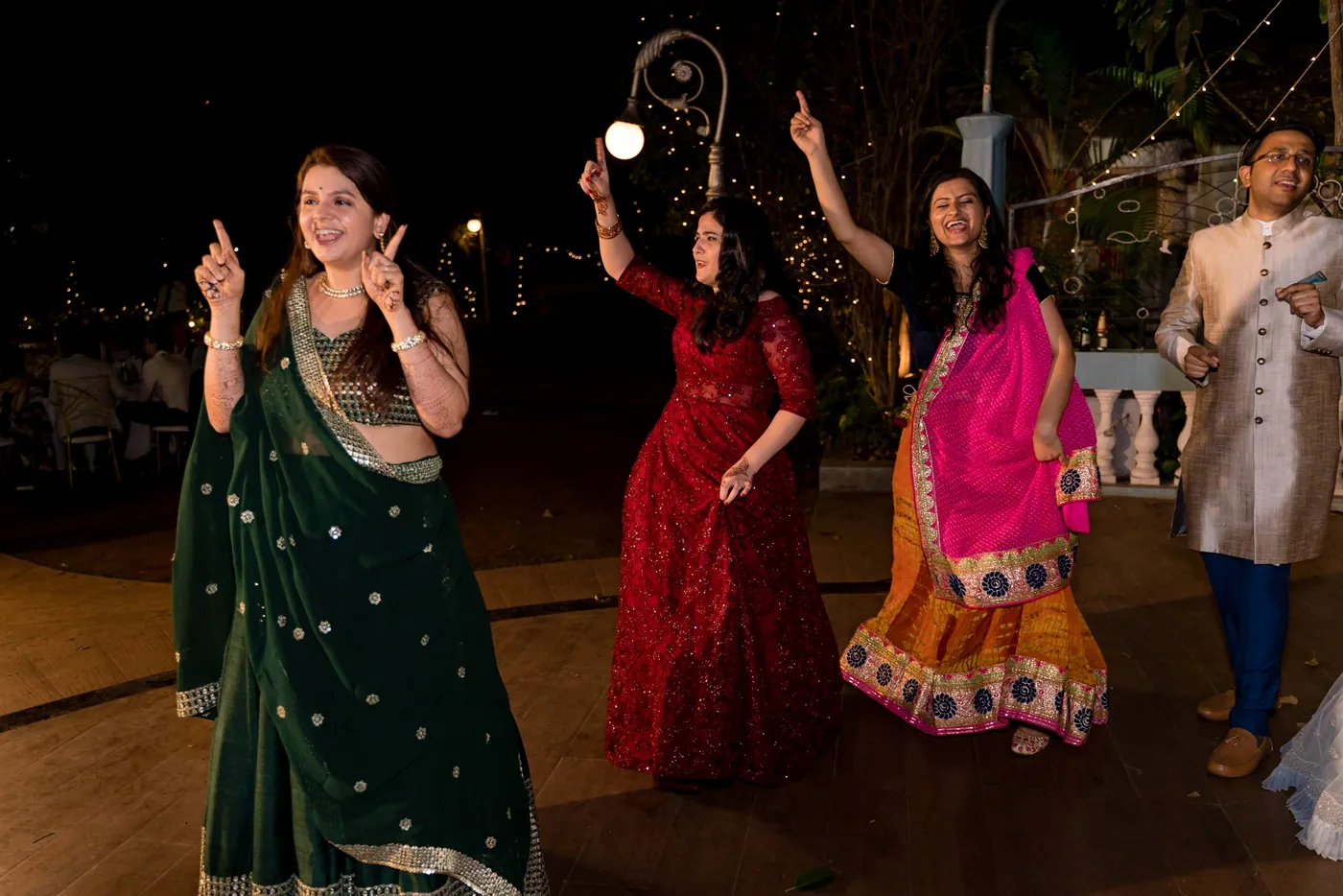Three women in green, red and pink lehengas dance with arms raised