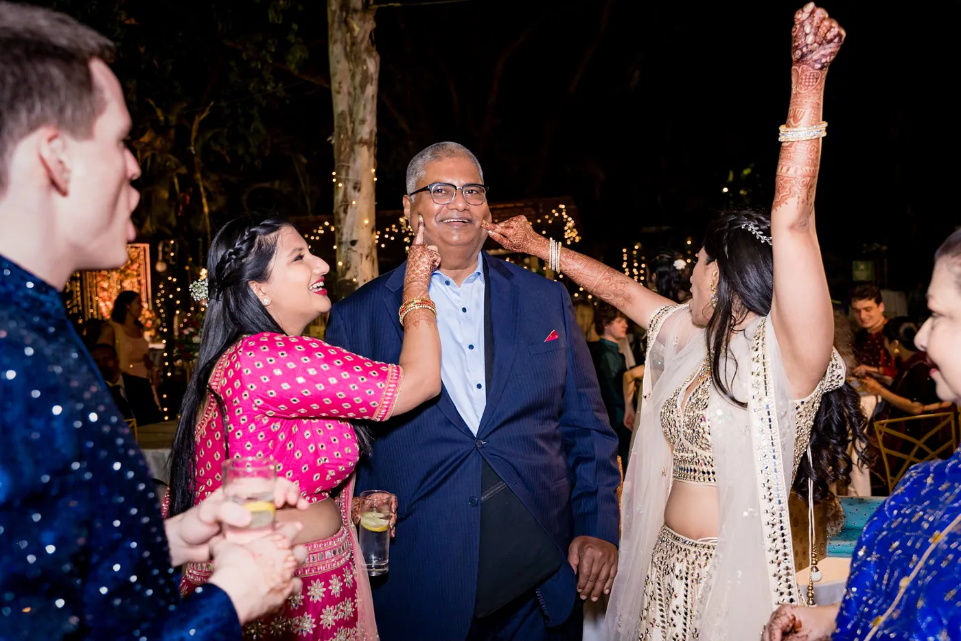 A man in a navy suit smiles as a woman in a pink saree pats his cheek