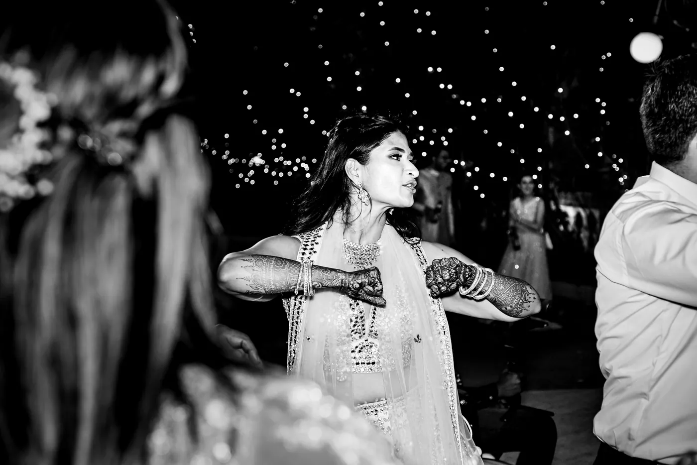 In black and white, Medha with a flower in her hair dances with hennaed hands near her face