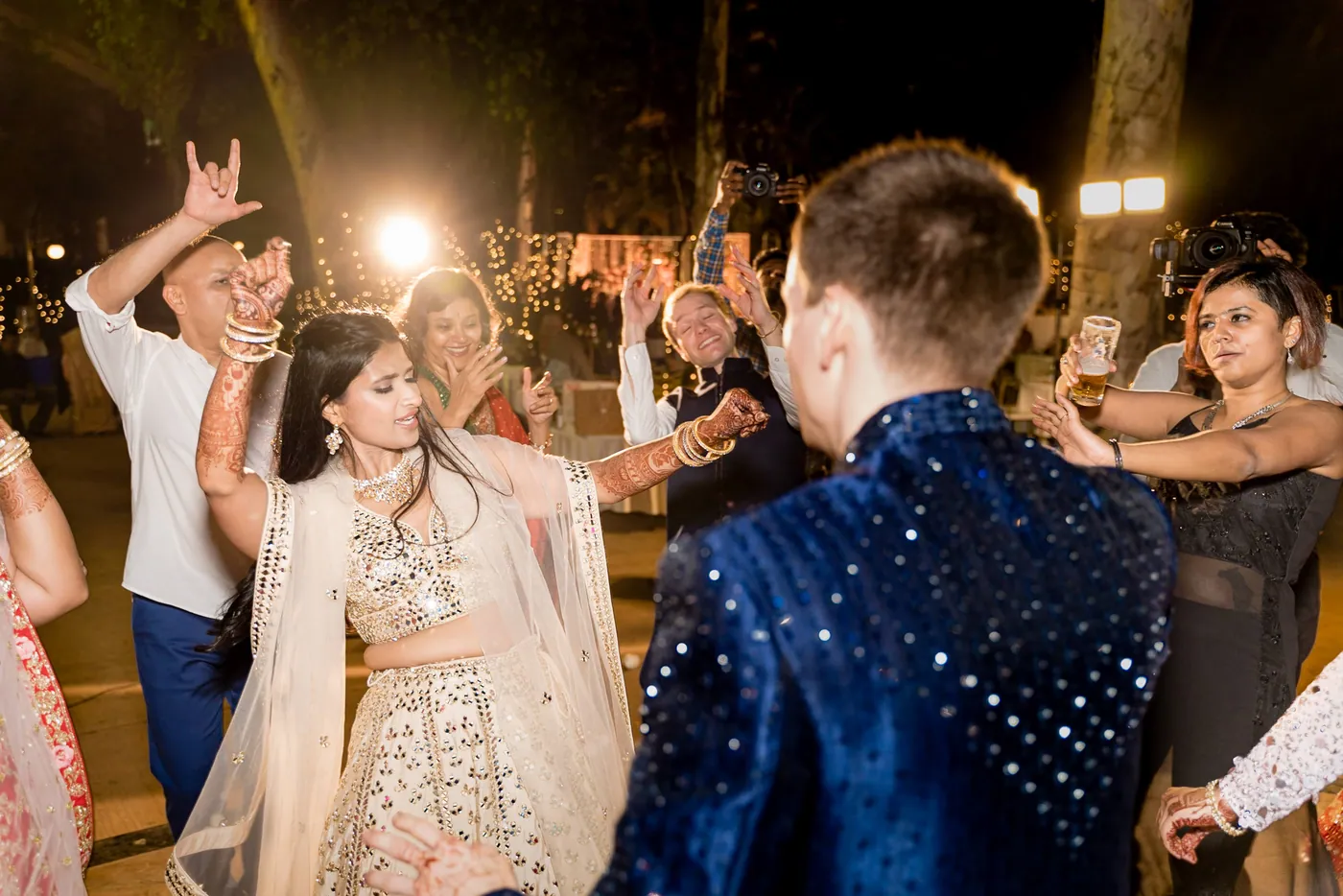 Medha dances in front of Stefan in his navy sherwani with guests dancing around them