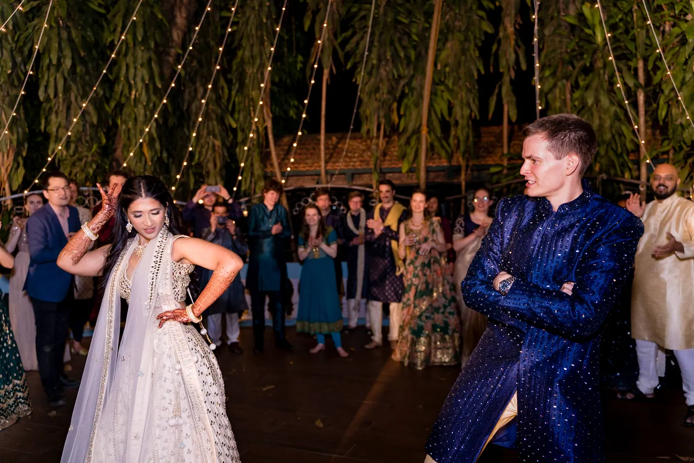 Medha strikes a pose, hand on hip, while Stefan stands with arms crossed and a crowd watches behind them